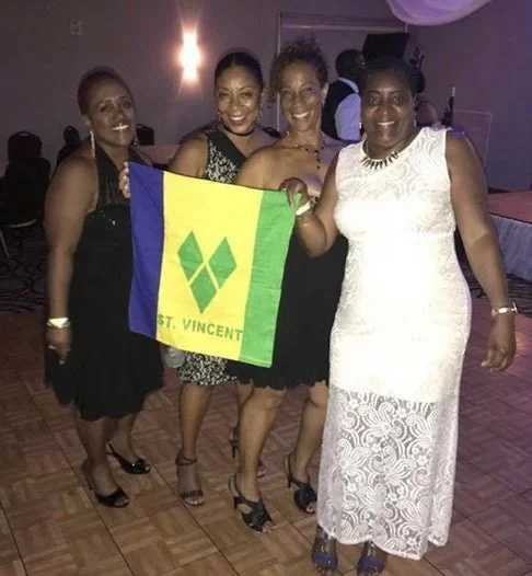Four women at a party holding a St. Vincent flag and smiling.