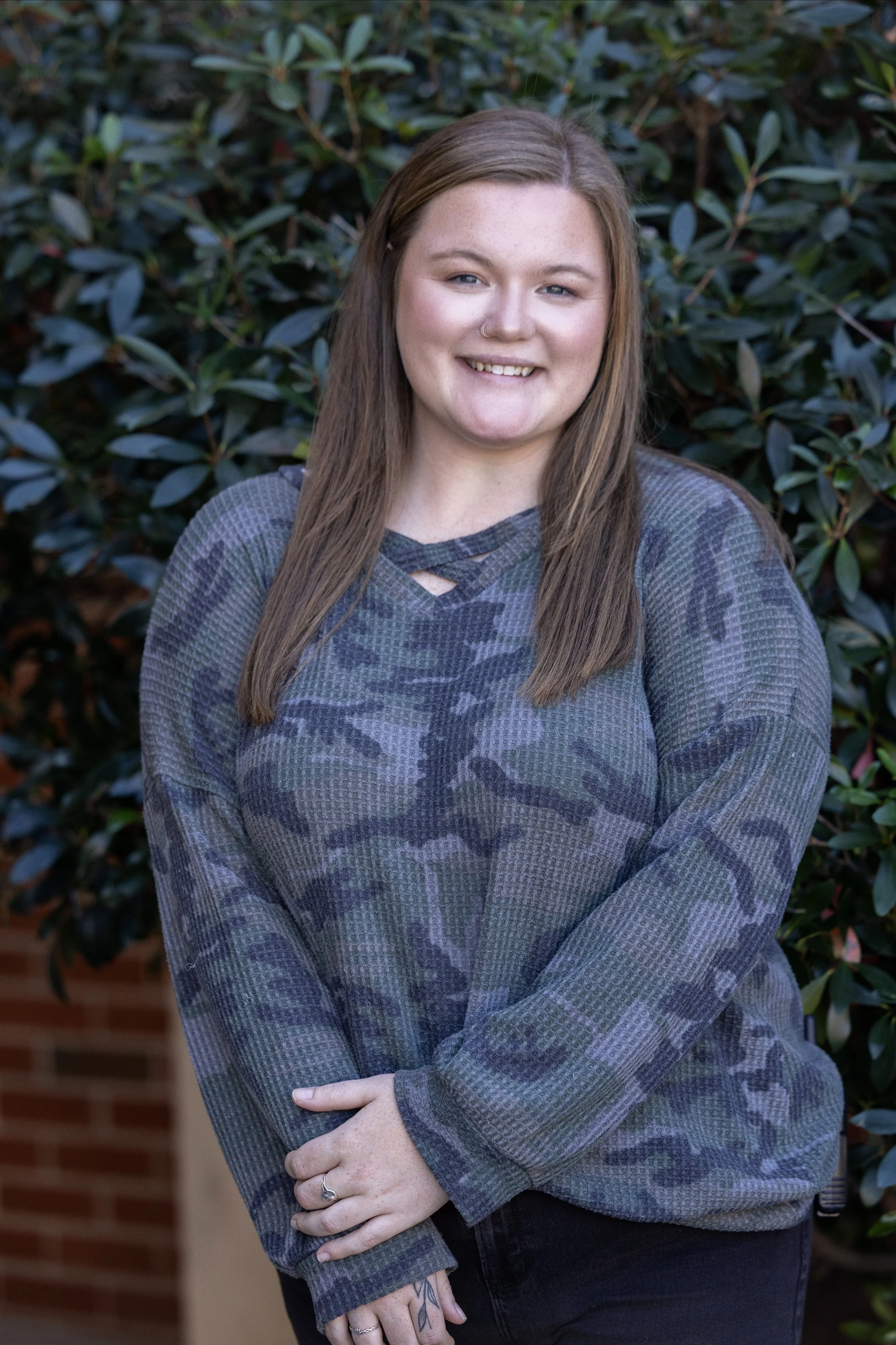 Person with long brown hair, wearing a plaid jacket and smiling against a neutral gray background.