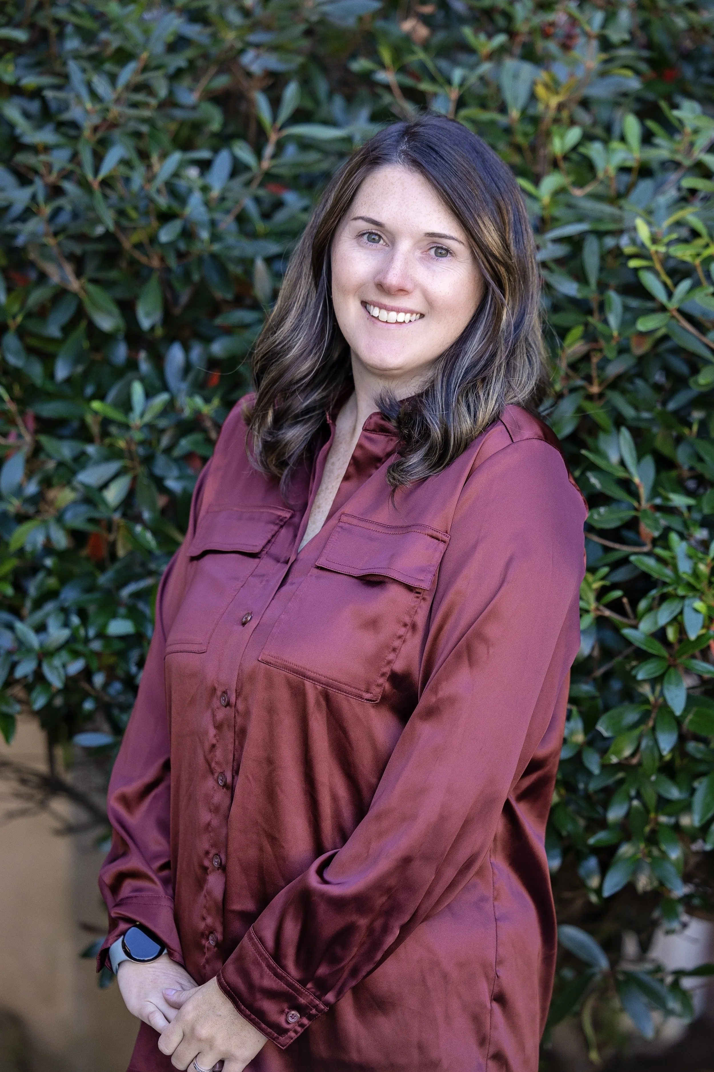 Woman with dark hair smiling, wearing a black top and green cardigan, against a gray background.