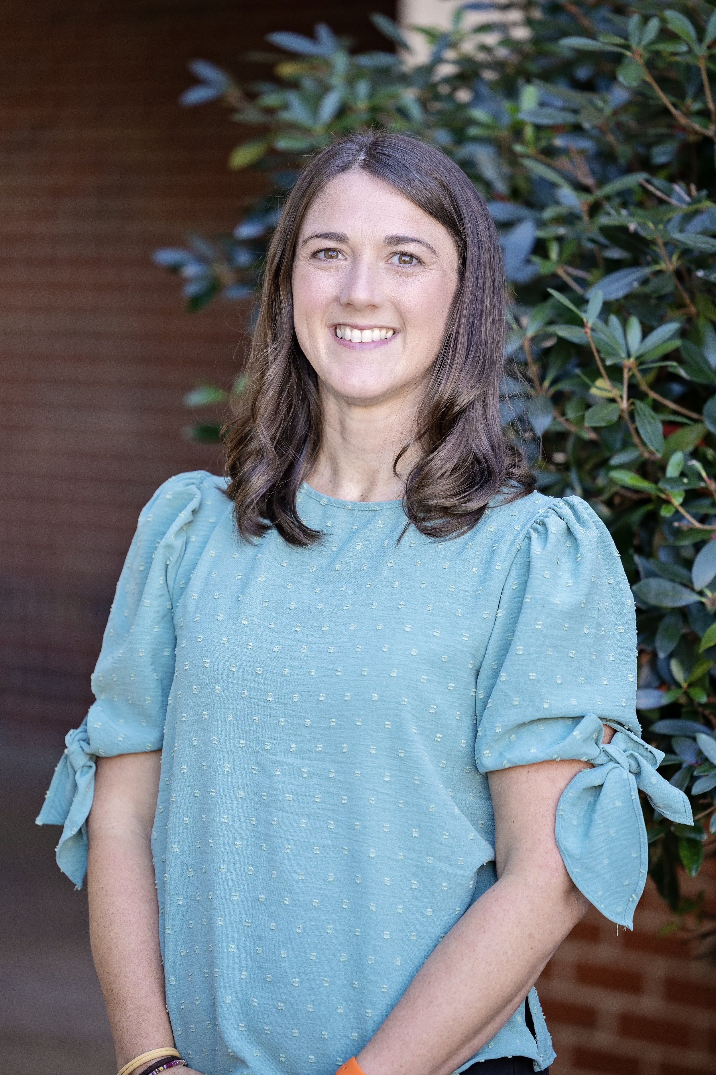 Smiling woman with long brown hair wearing a light blue sweater against a light gray background.
