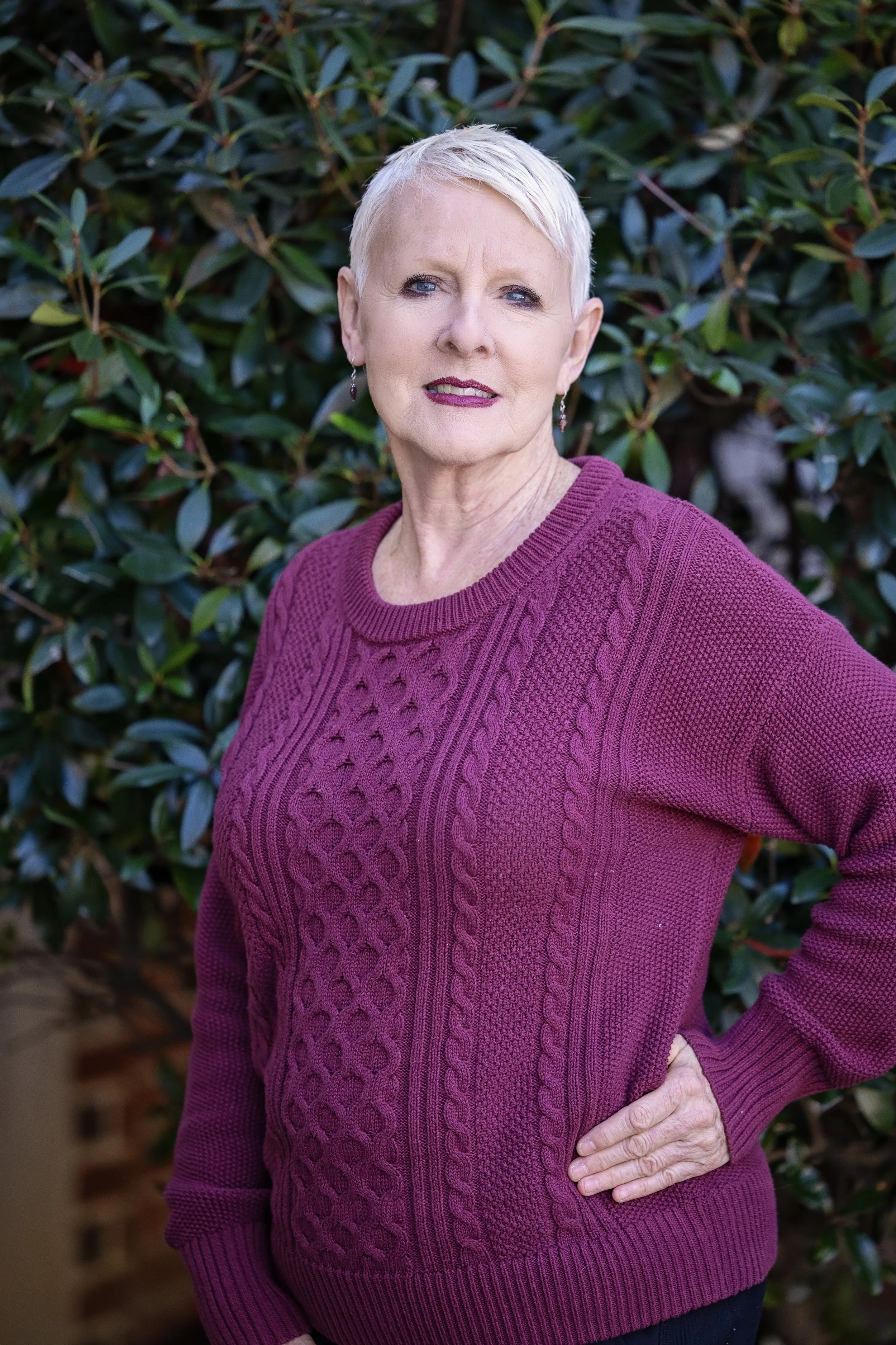 Woman with short white hair wearing a floral blouse and pearl earrings, smiling against a light gray background.