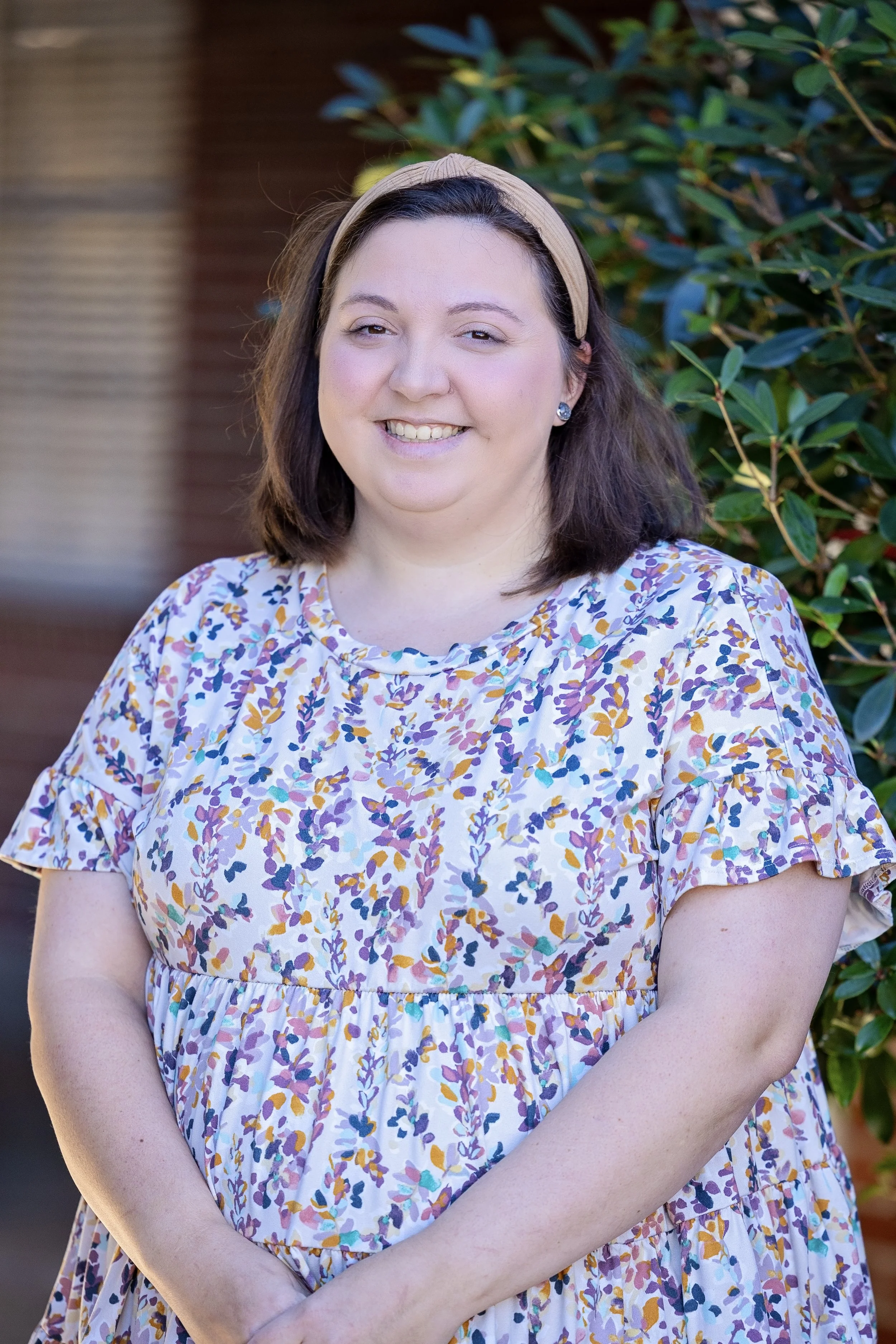 Smiling person with curly hair wearing a colorful top against a gray background.