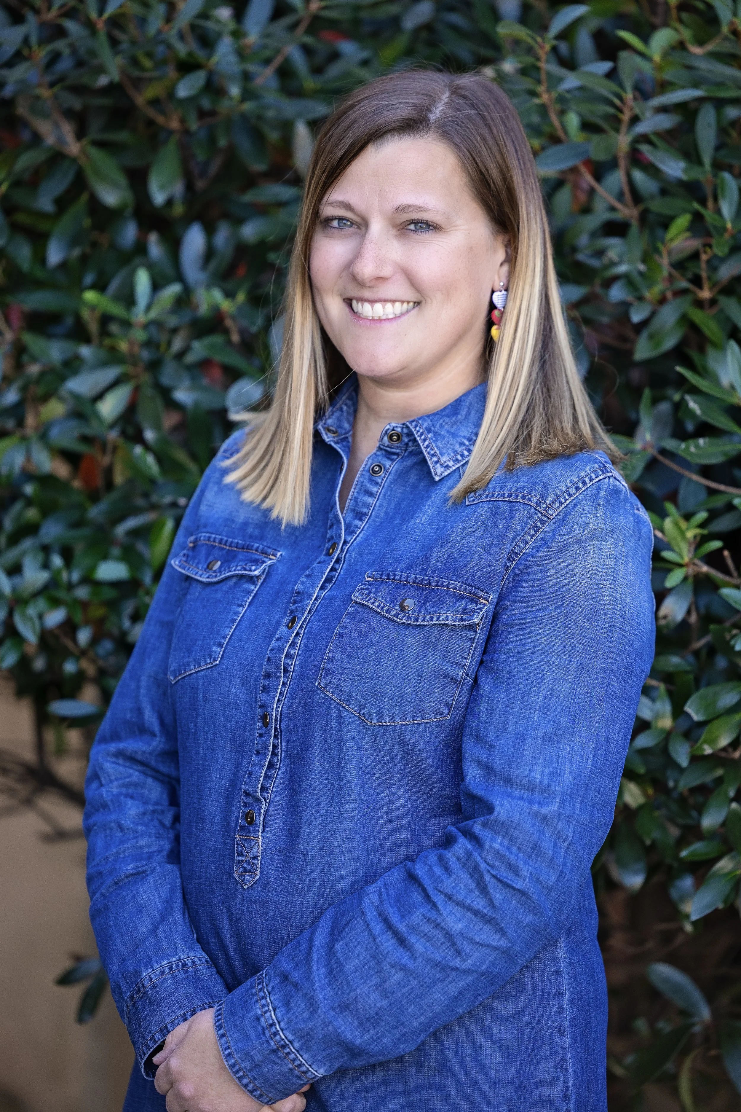 Smiling person with long hair wearing a green top and a headband against a gray background.
