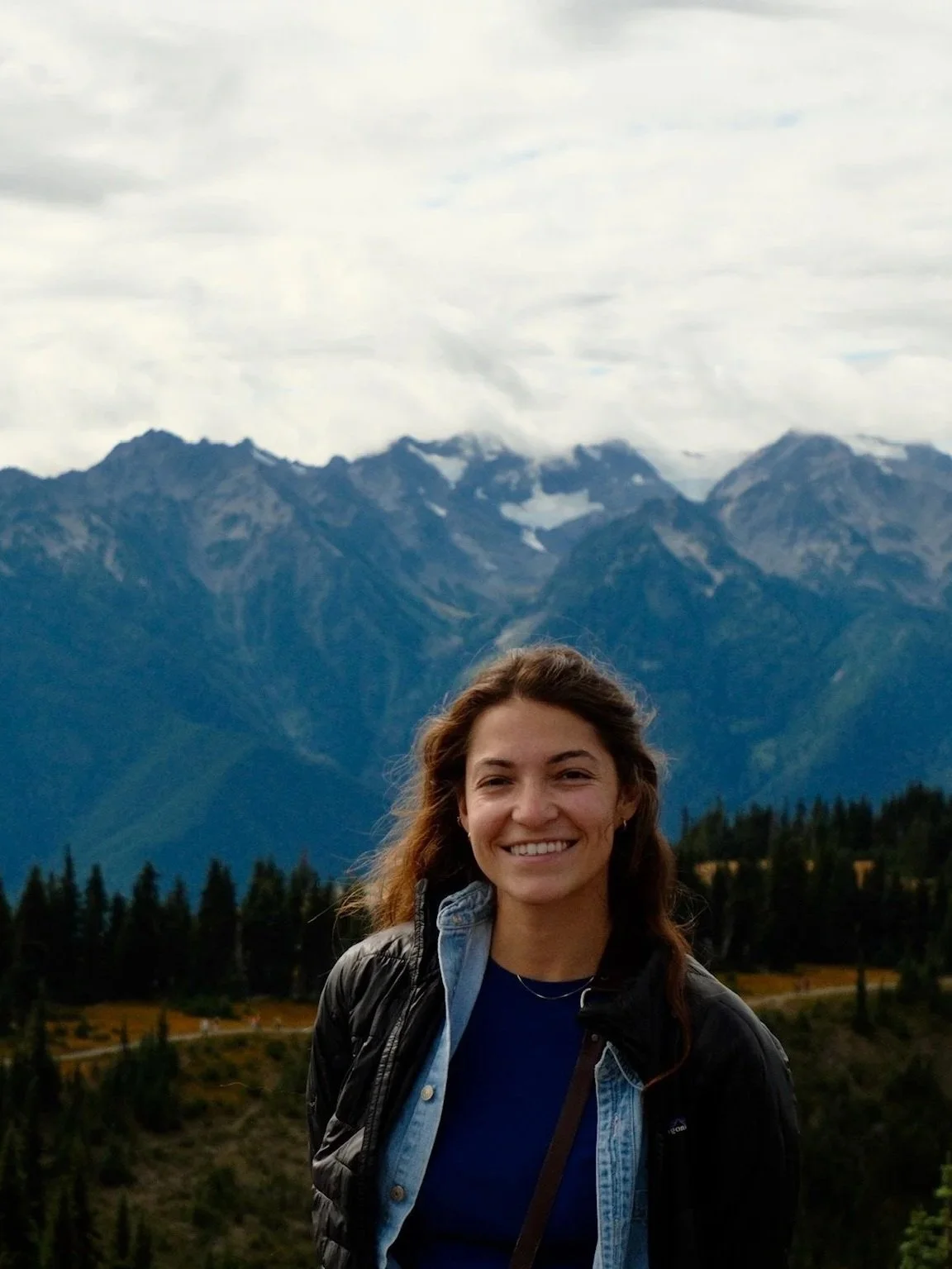 Young woman smiling outdoors with mountain range and cloudy sky in the background in olympic national park.