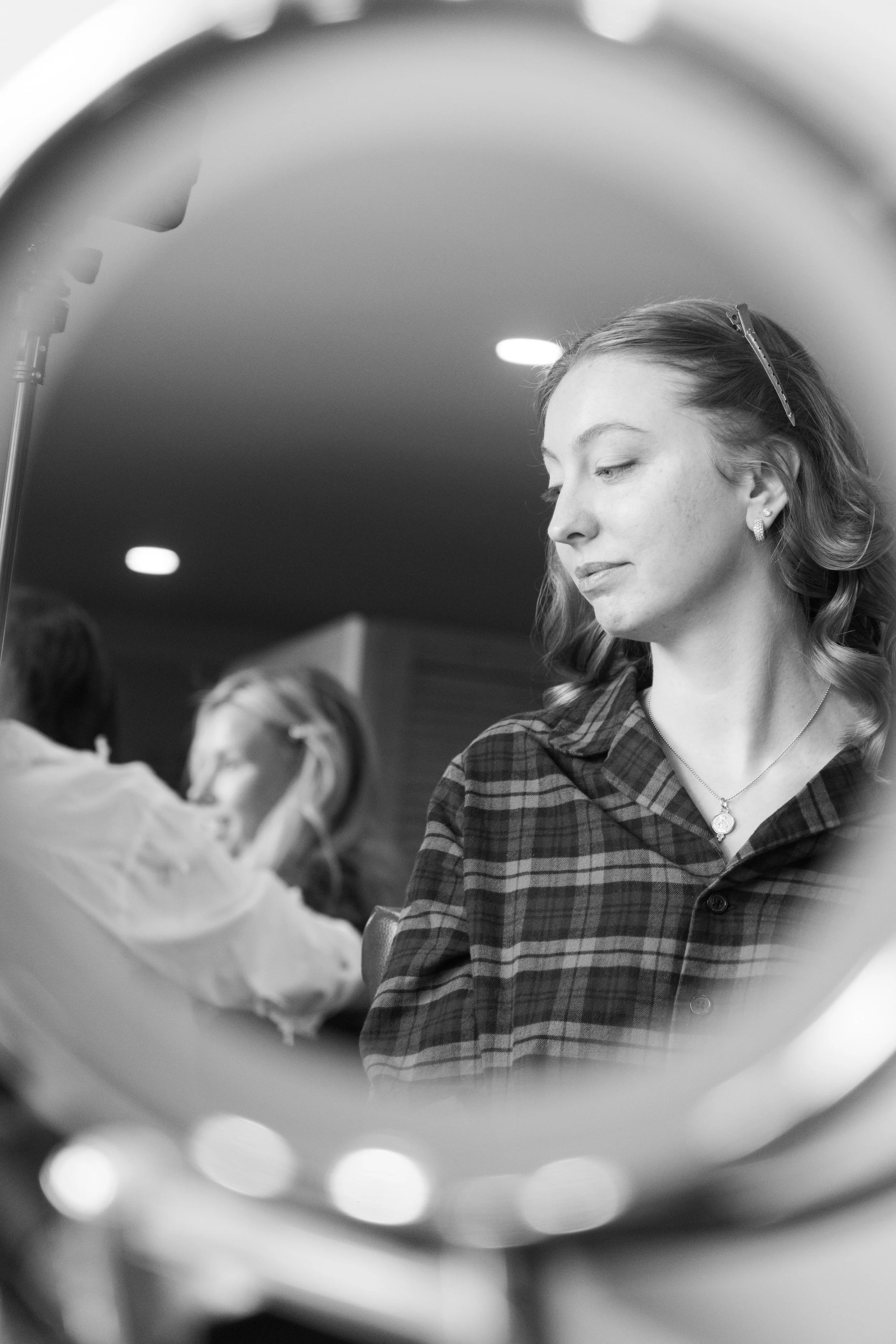A woman looking at herself in a mirror, with other people blurred in the background.