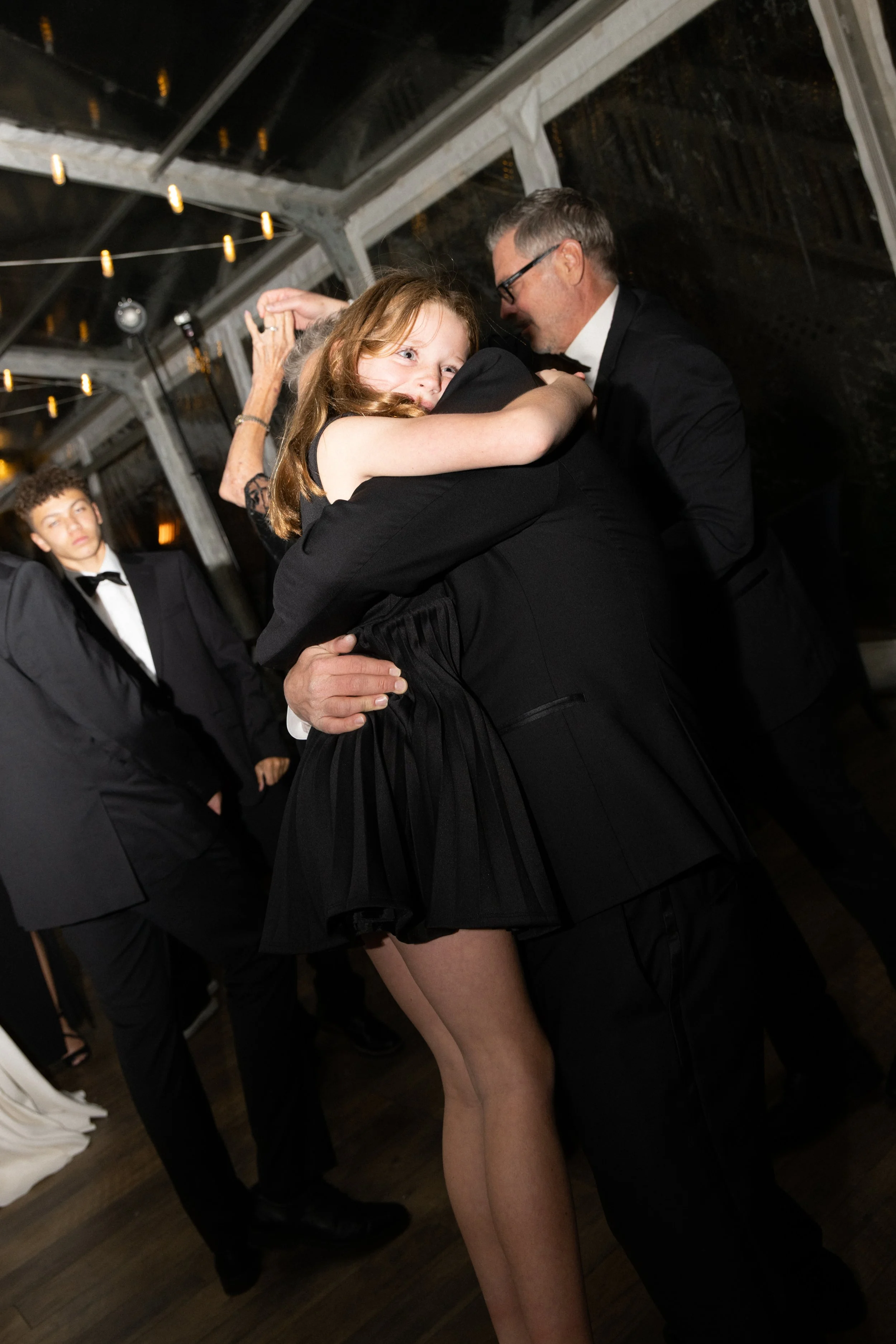 A young girl with red hair hugging a man in a tuxedo at a formal event or dance.