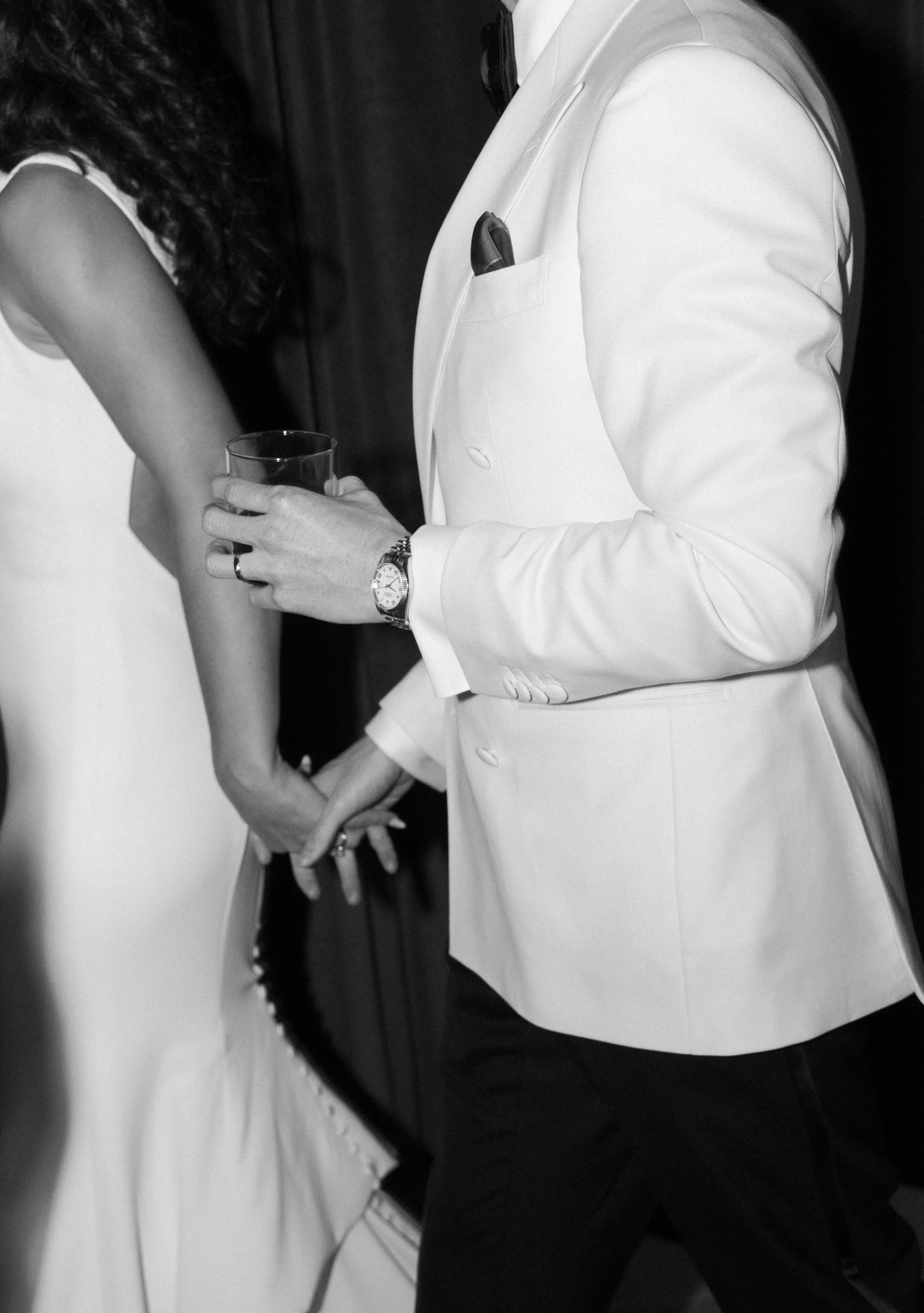 Close-up of a man in a white tuxedo holding a glass and a woman in a white dress at an event.