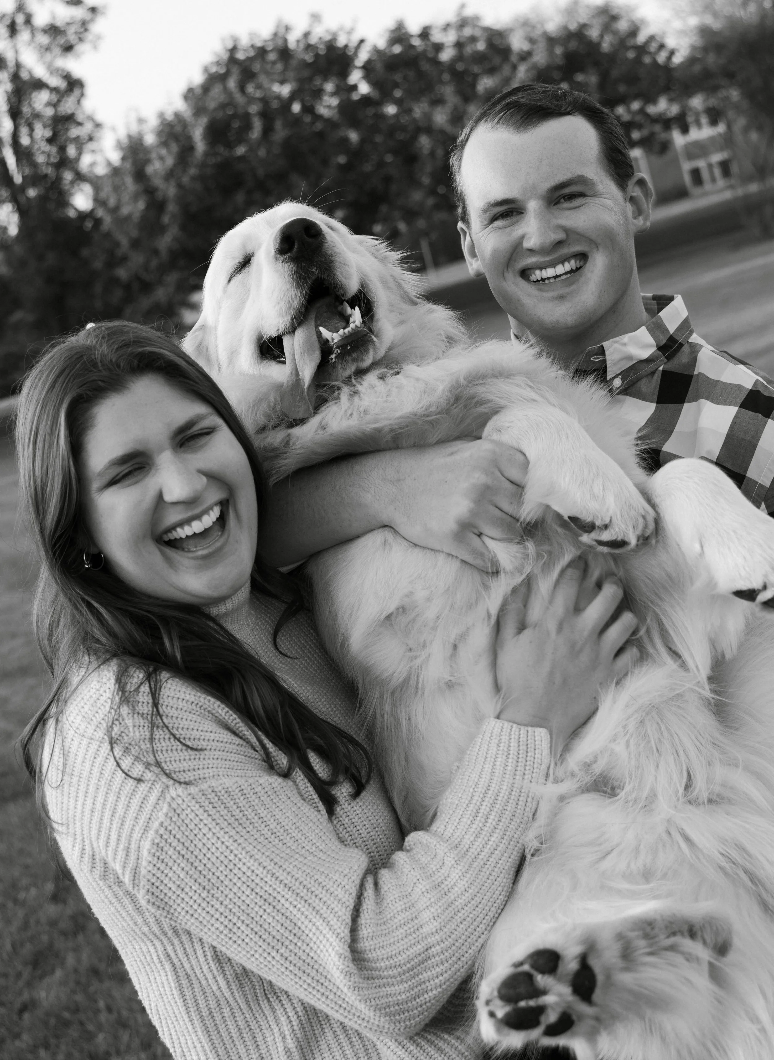 A happy couple holding a large, joyful golden retriever dog outdoors.