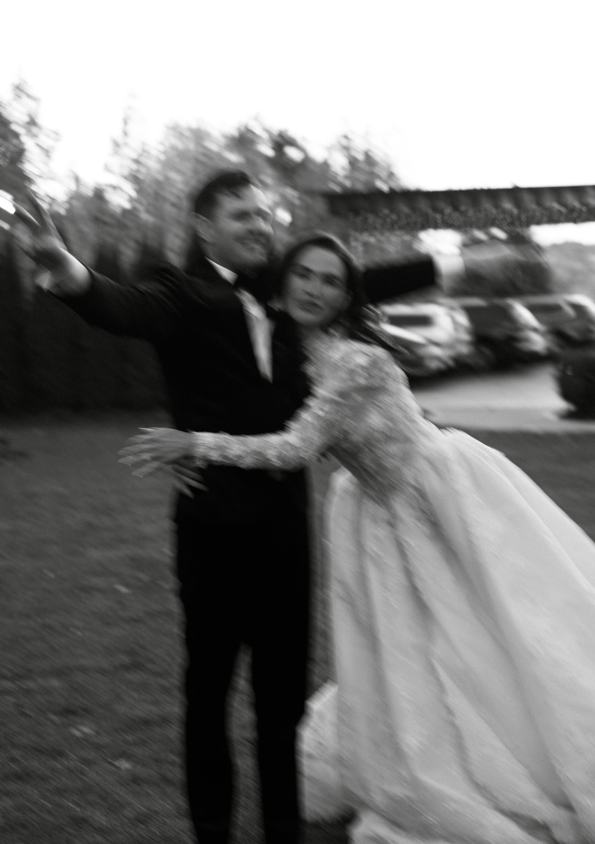 Blurred black and white photo of a man and woman embracing outdoors, with cars and trees in the background.