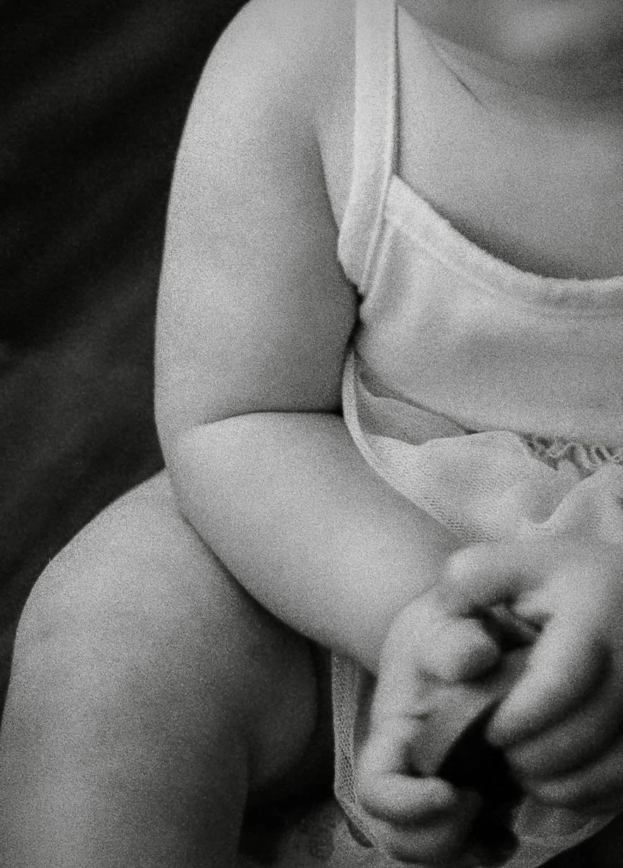 Close-up black and white photo of a child's torso, arm, and hand holding an object, with the child wearing a sleeveless top.