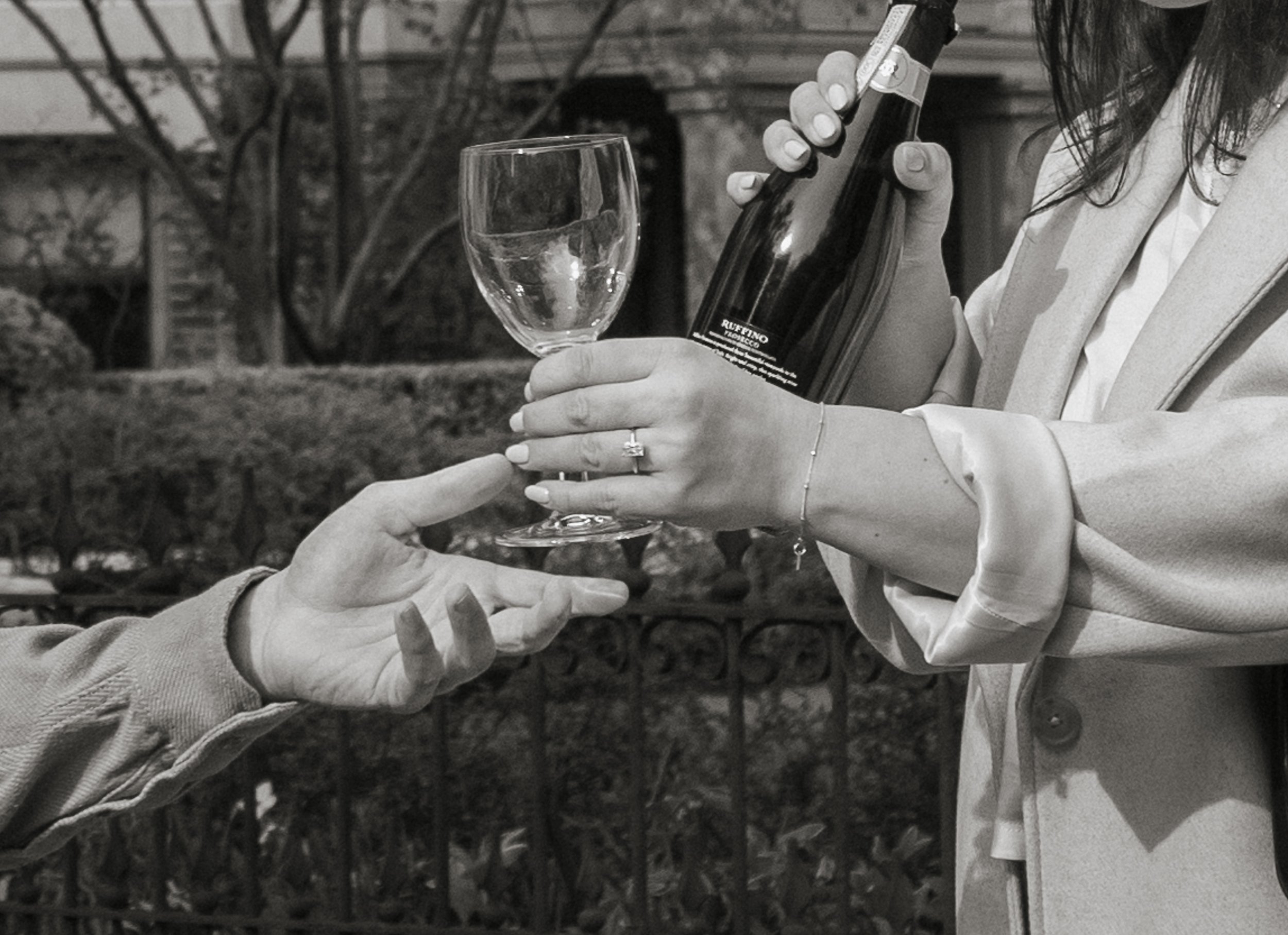 A woman is pouring wine from a bottle into a glass held by another person in an outdoor setting.