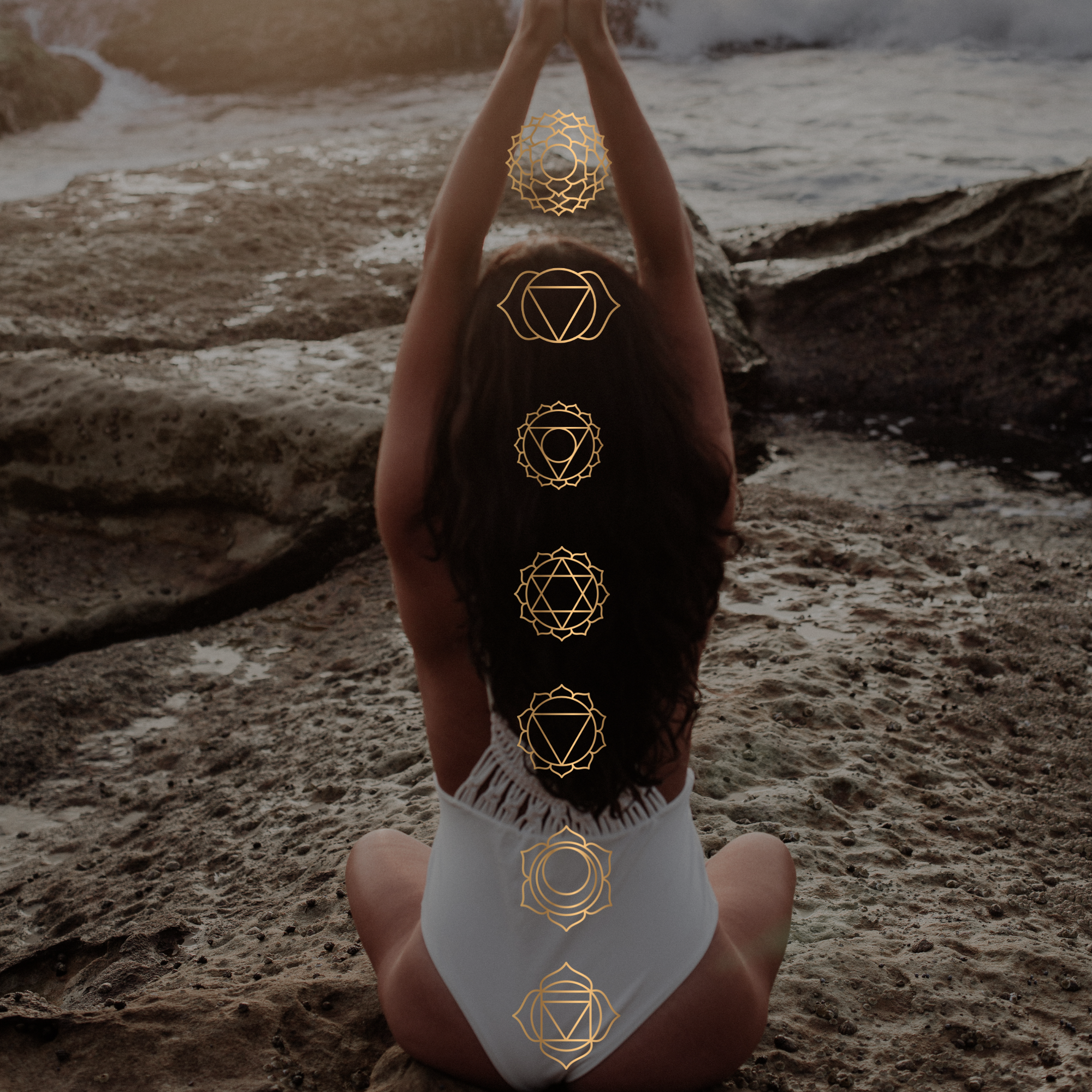 Woman in white swimsuit meditating on rocky beach with chakra symbols