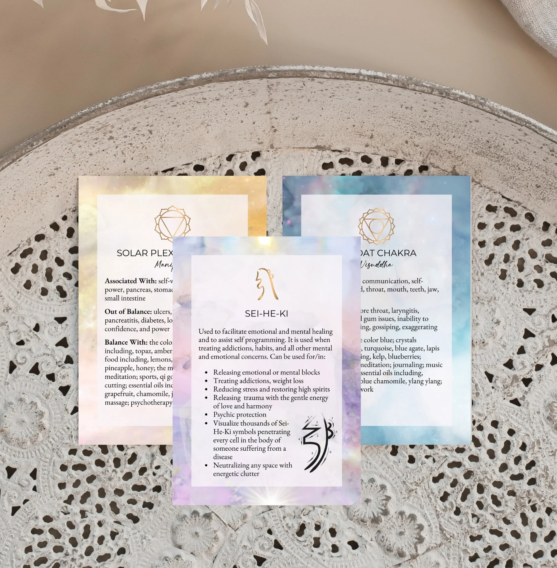 Three spiritual cards on a lace table: one featuring the Solar Plexus Chakra, another the Throat Chakra, and the third with the symbol Sei-He-Ki for emotional healing. Each card describes associated traits, imbalances, and balancing methods.