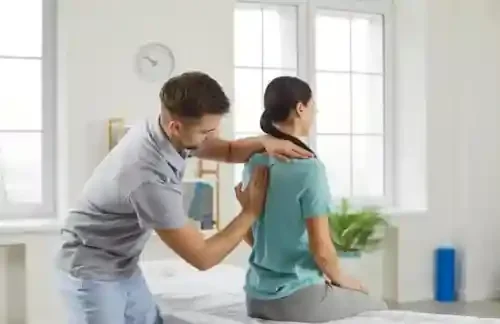 Chiropractor adjusting a woman's shoulder in a well-lit medical office.
