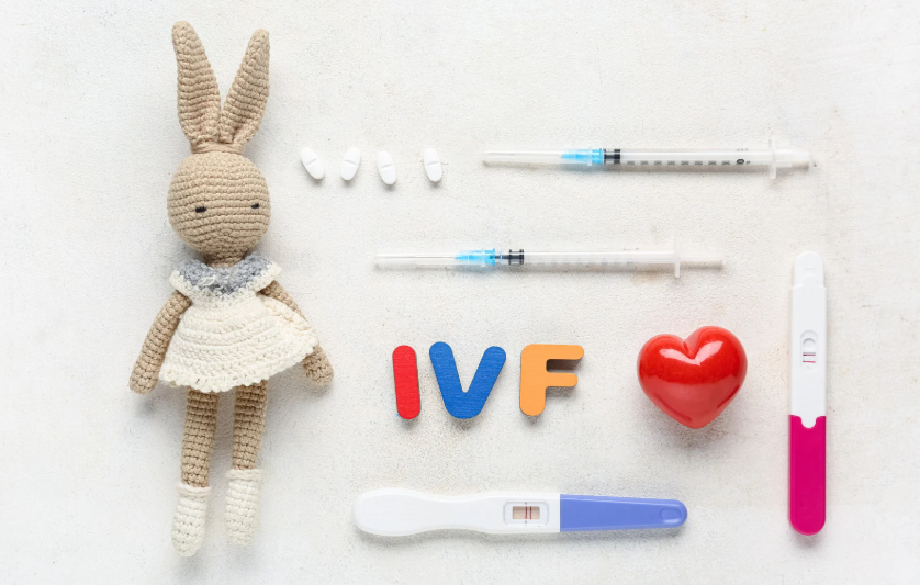 Crocheted bunny toy with IVF-related medical items, including pills, syringes, a thermometer, and colorful letters spelling 'IVF', on a white background.
