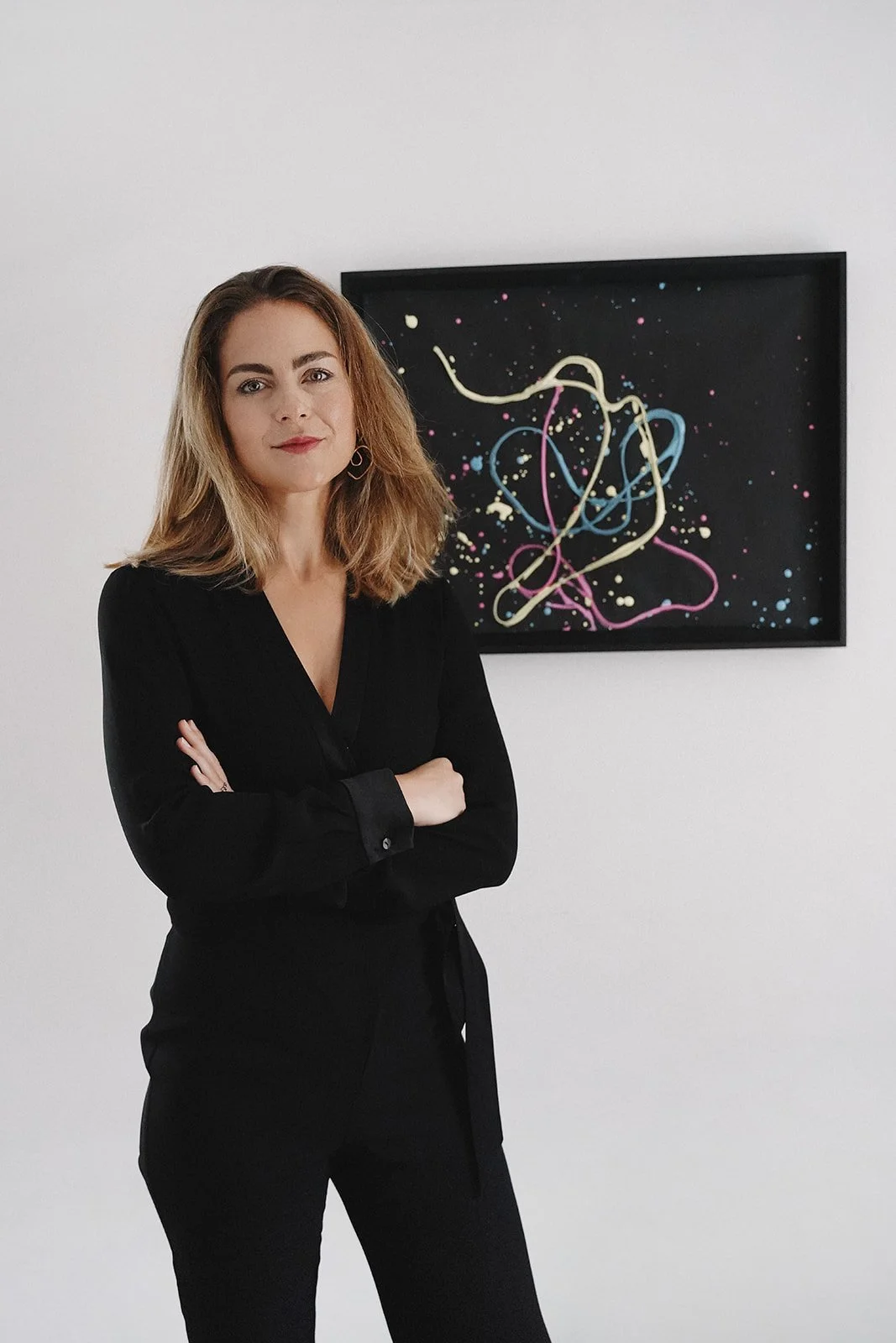 Maria-Anna Messner-Haidenthaler standing with arms crossed in front of abstract artwork.