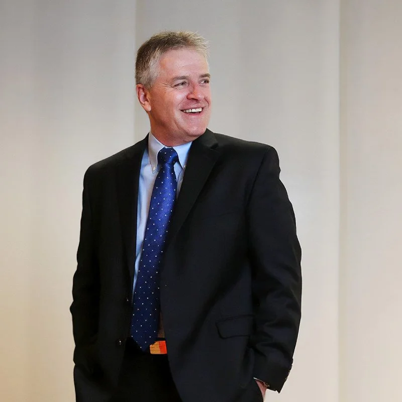 Bob is standing, wearing a suit. He is smiling, looking right, off camera.