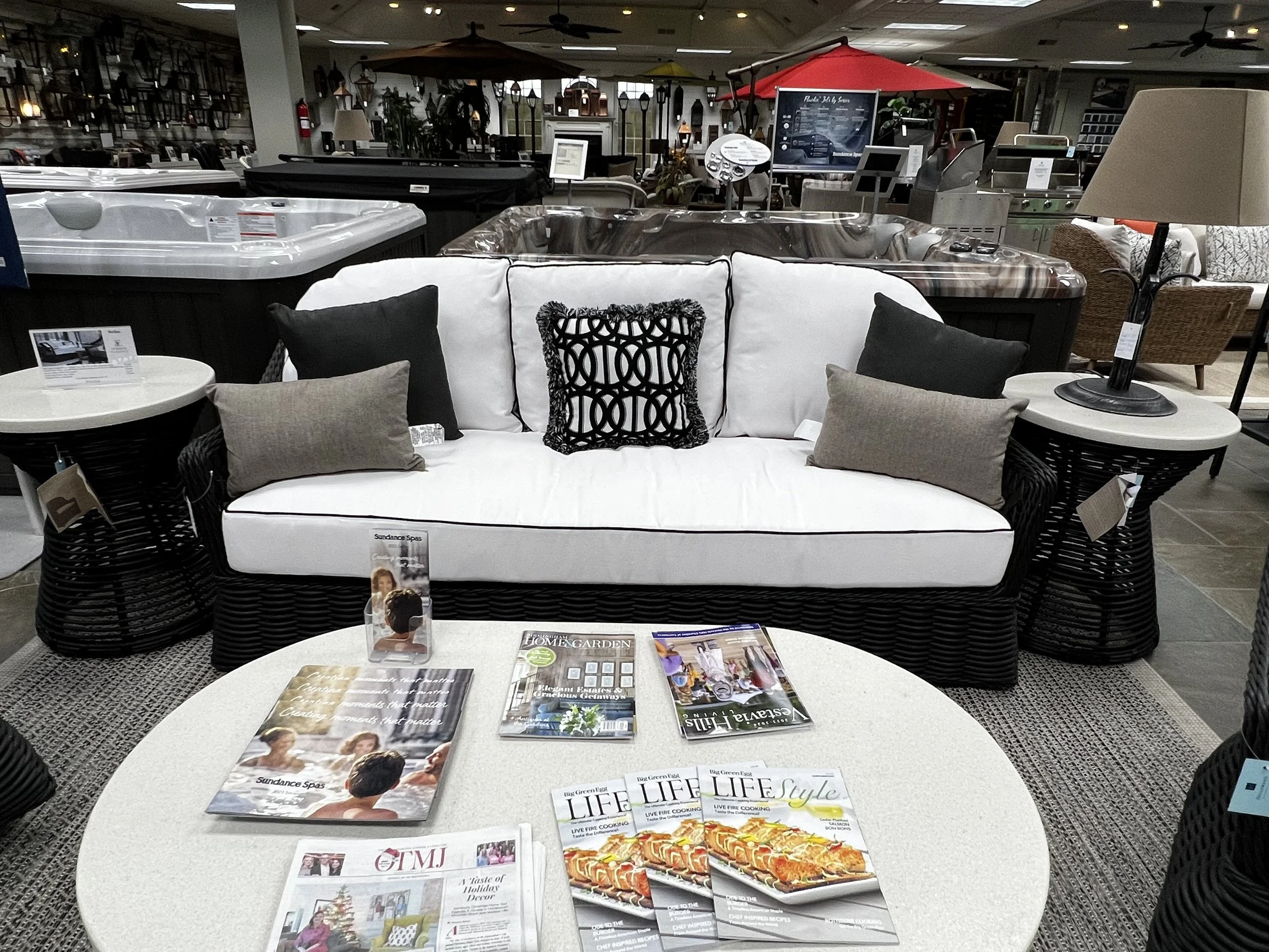 Black wicker sofa with white cushions, black and grey throw pillows, and a white coffee table inside of Hollywood Outdoor Living's store