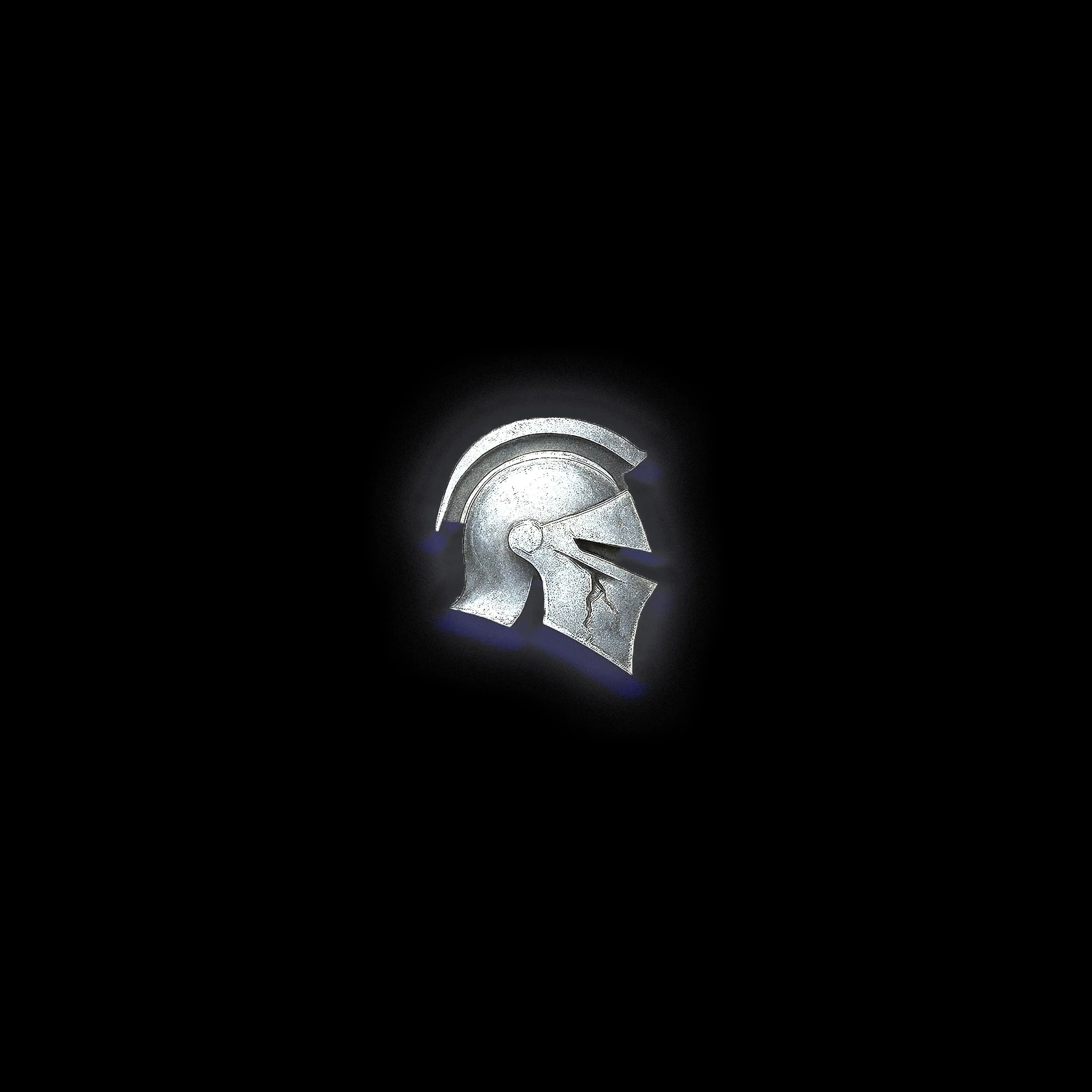 Silver metallic Spartan helmet with cracks, illuminated against a black background.