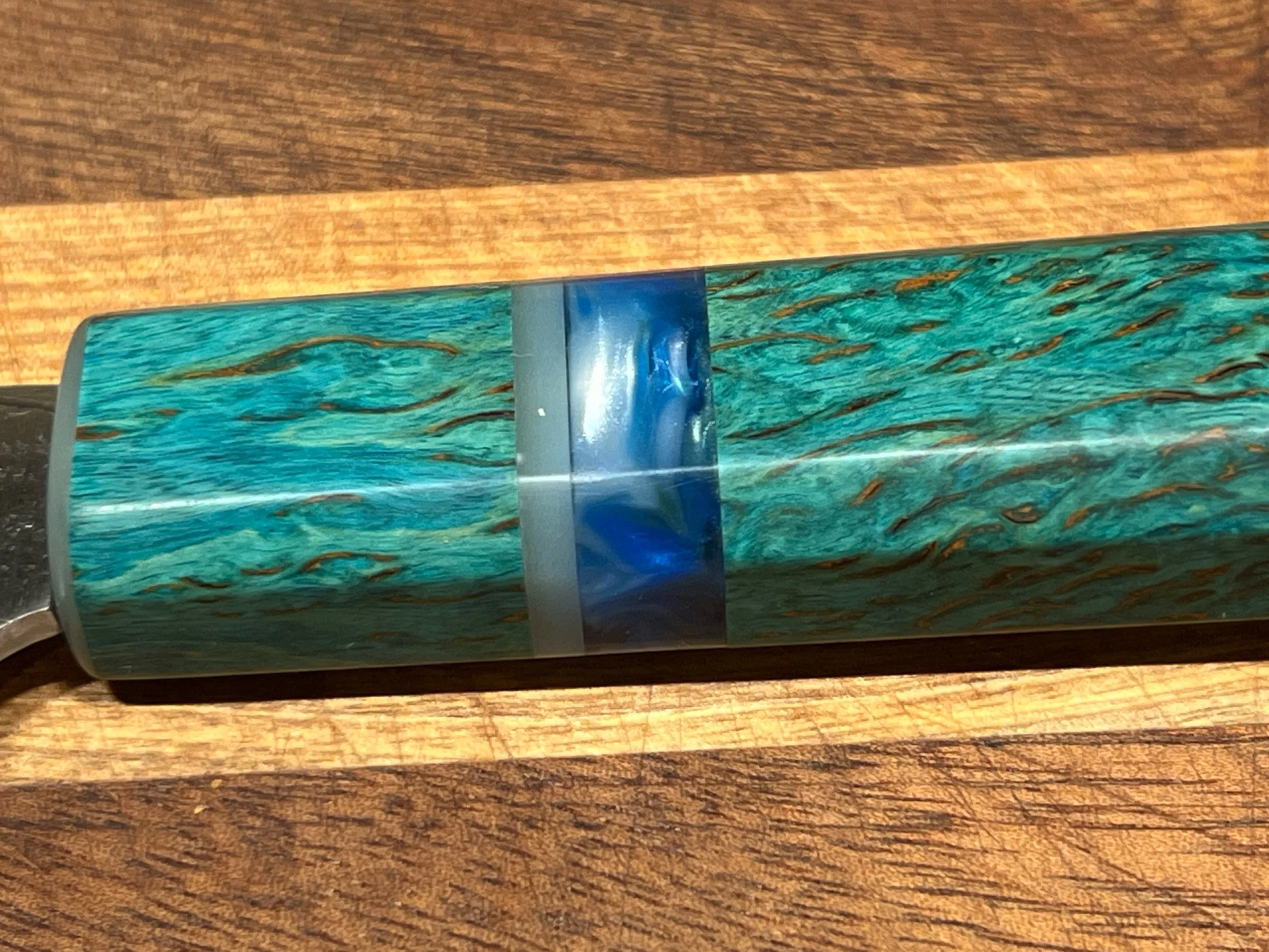 Close-up of a decorative glass object with a blue base and swirling patterns of green, orange, and black, resting on a wooden surface.