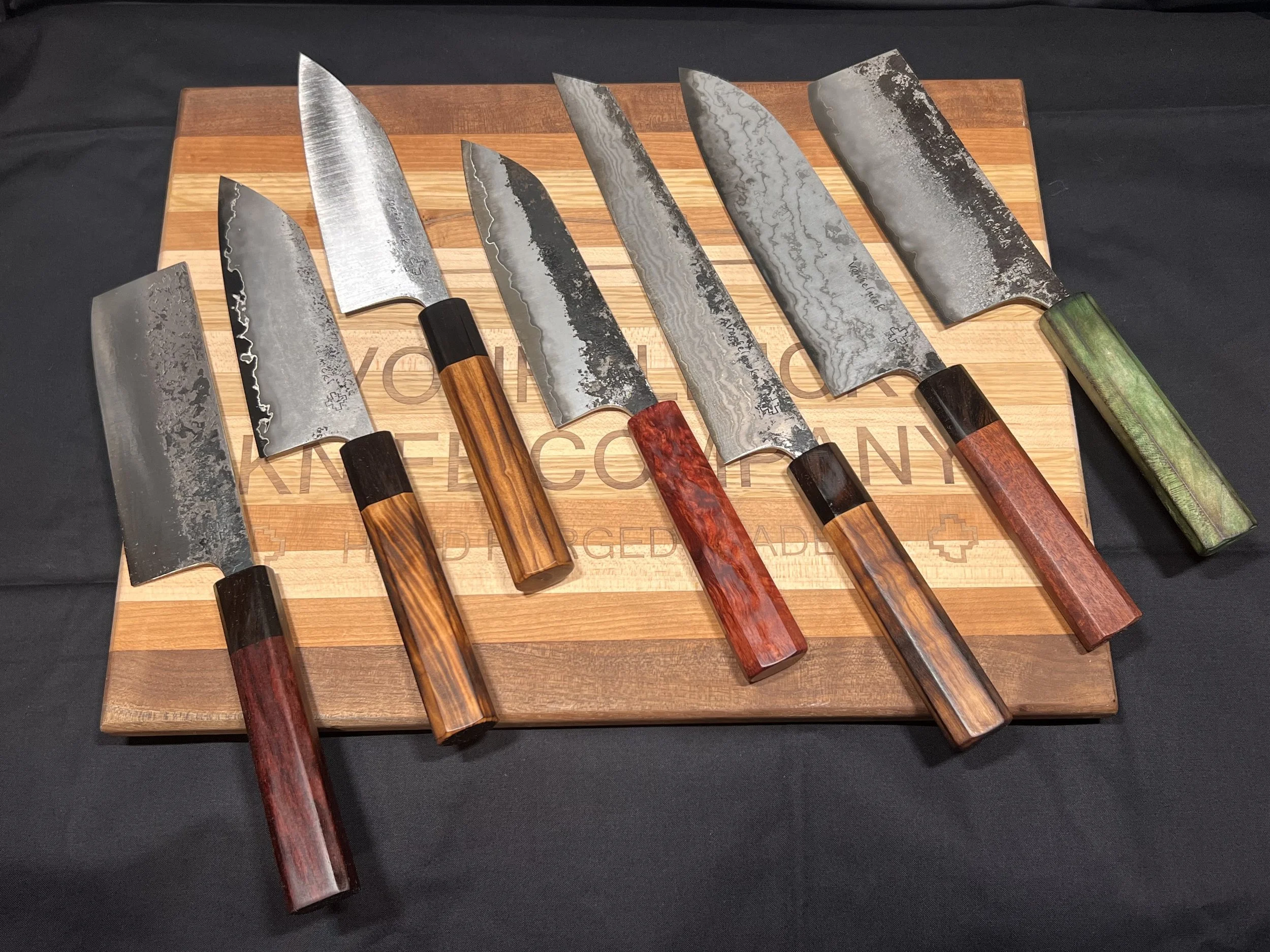 Set of six Japanese-style knives with patterned blades and colorful handles on a wooden cutting board.