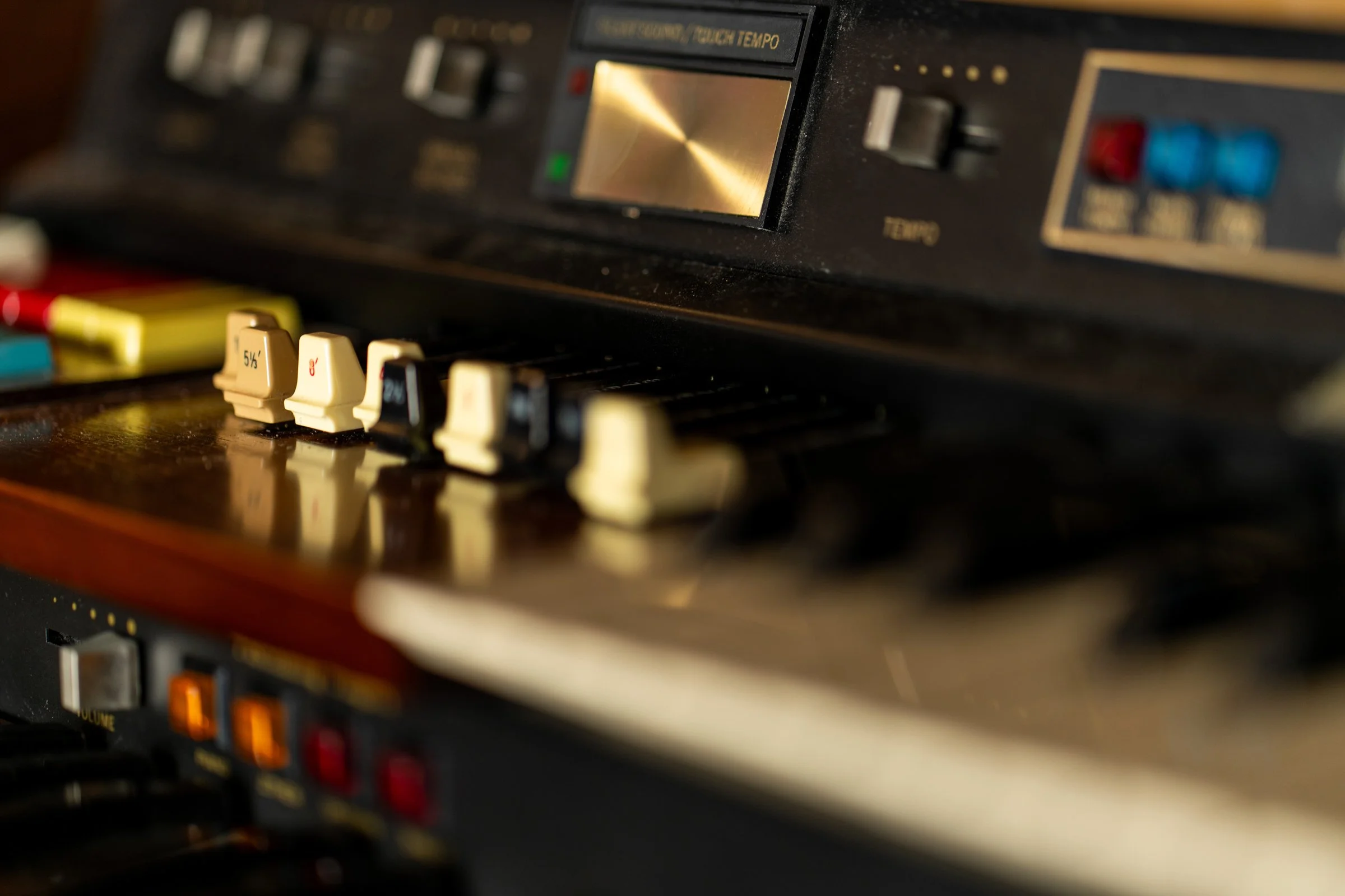 Close-up of a vintage black electronic music keyboard or synthesizer with various control knobs and colorful buttons.