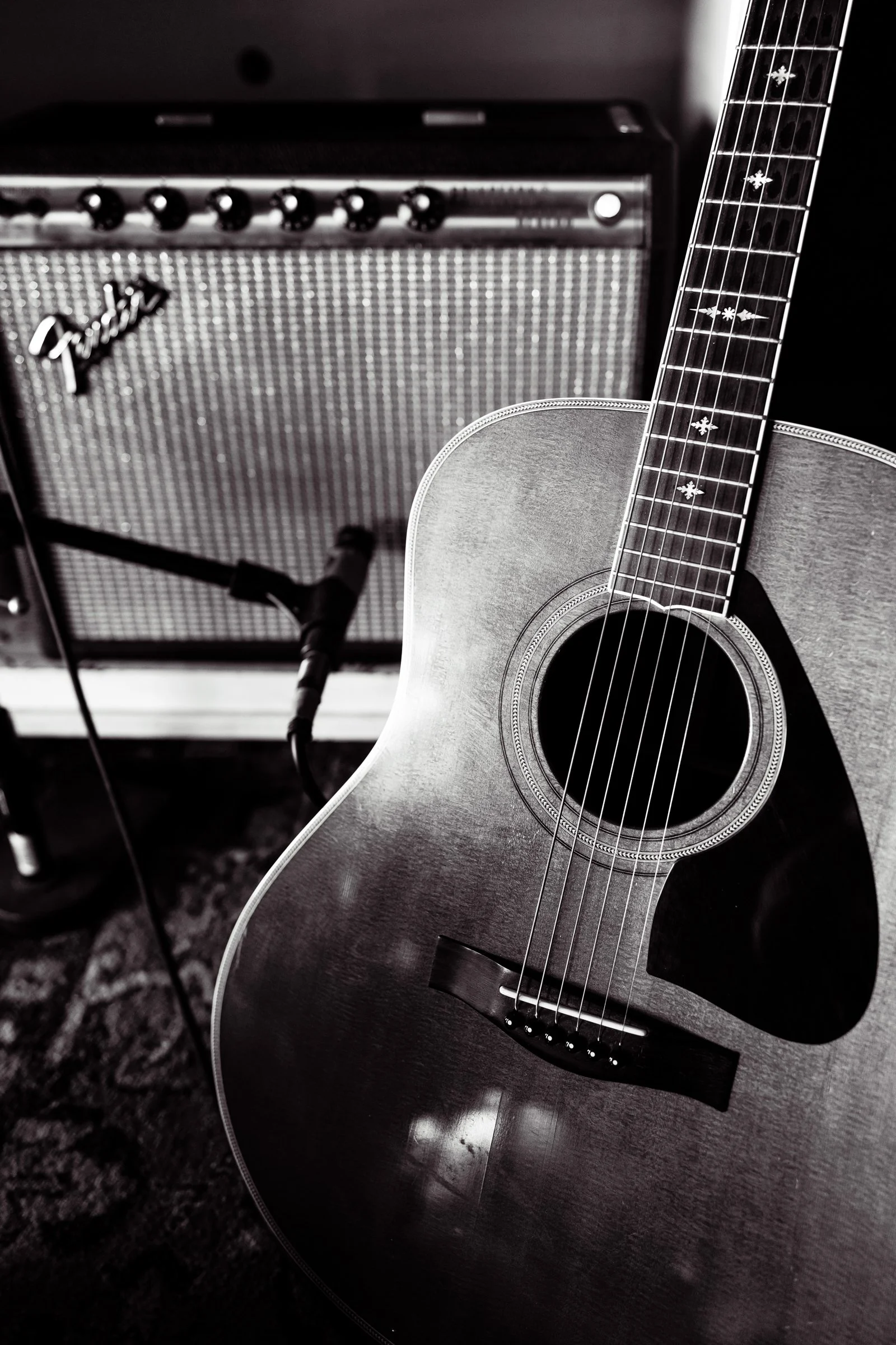 A black and white photo of an acoustic guitar leaning against a speaker cabinet in a music studio.