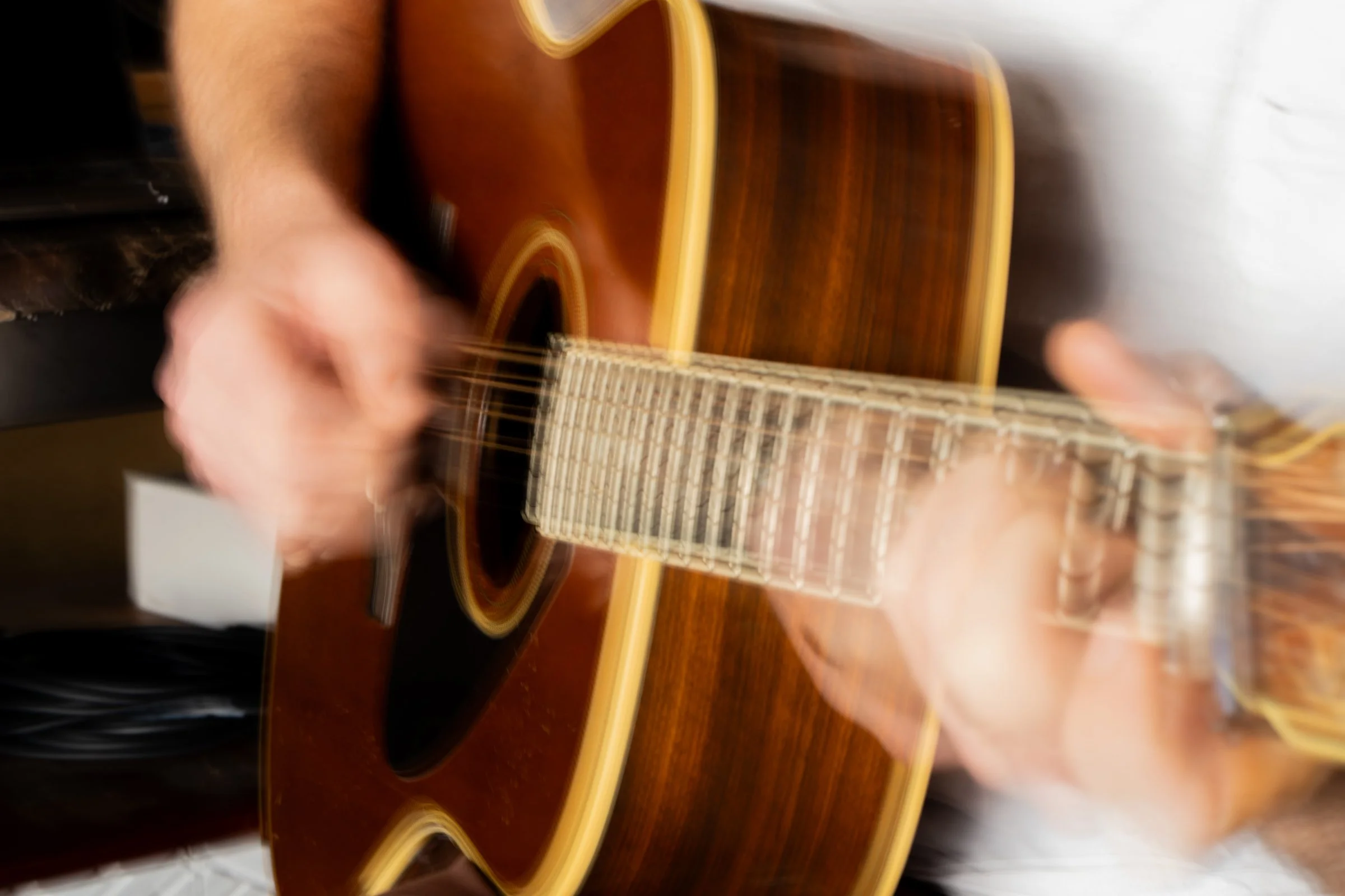 Blurry image of a person playing an acoustic guitar, with motion blur indicating movement of the hands and guitar strings.