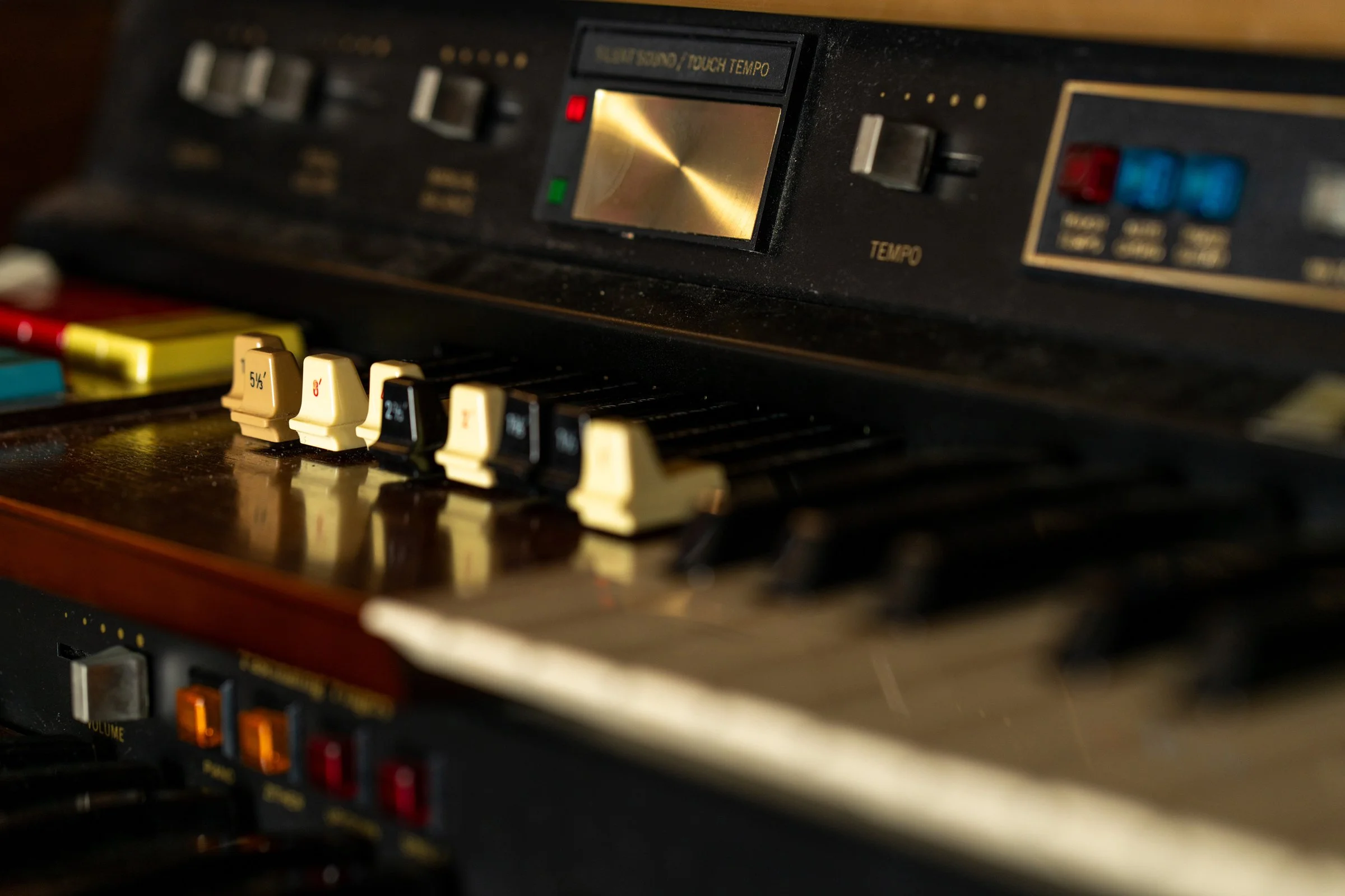 Close-up of a vintage keyboard synthesizer with black and white keys and control knobs, buttons, and display panel on top.