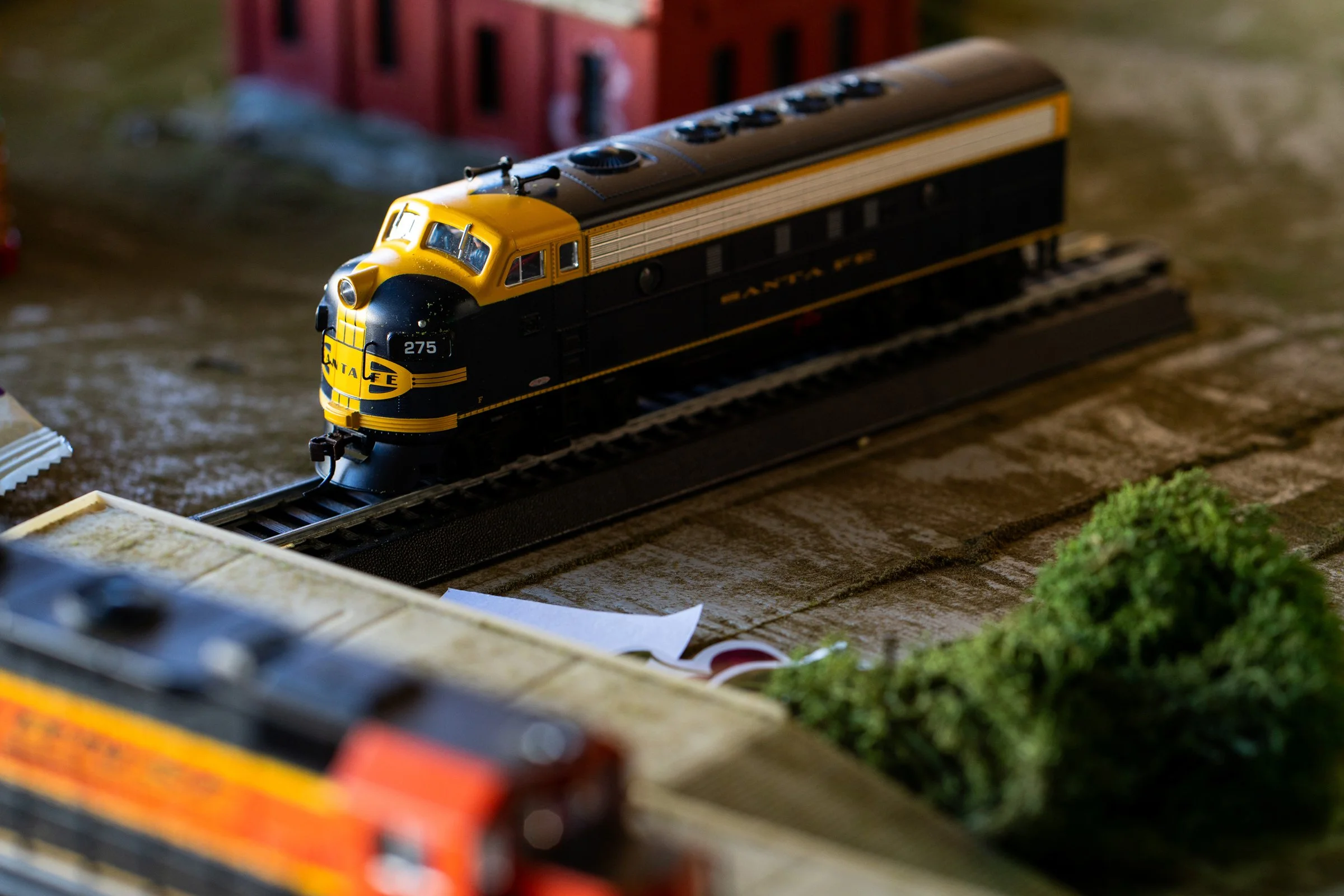 Model train setup with a yellow and black Santa Fe locomotive on tracks surrounded by miniature buildings and greenery.