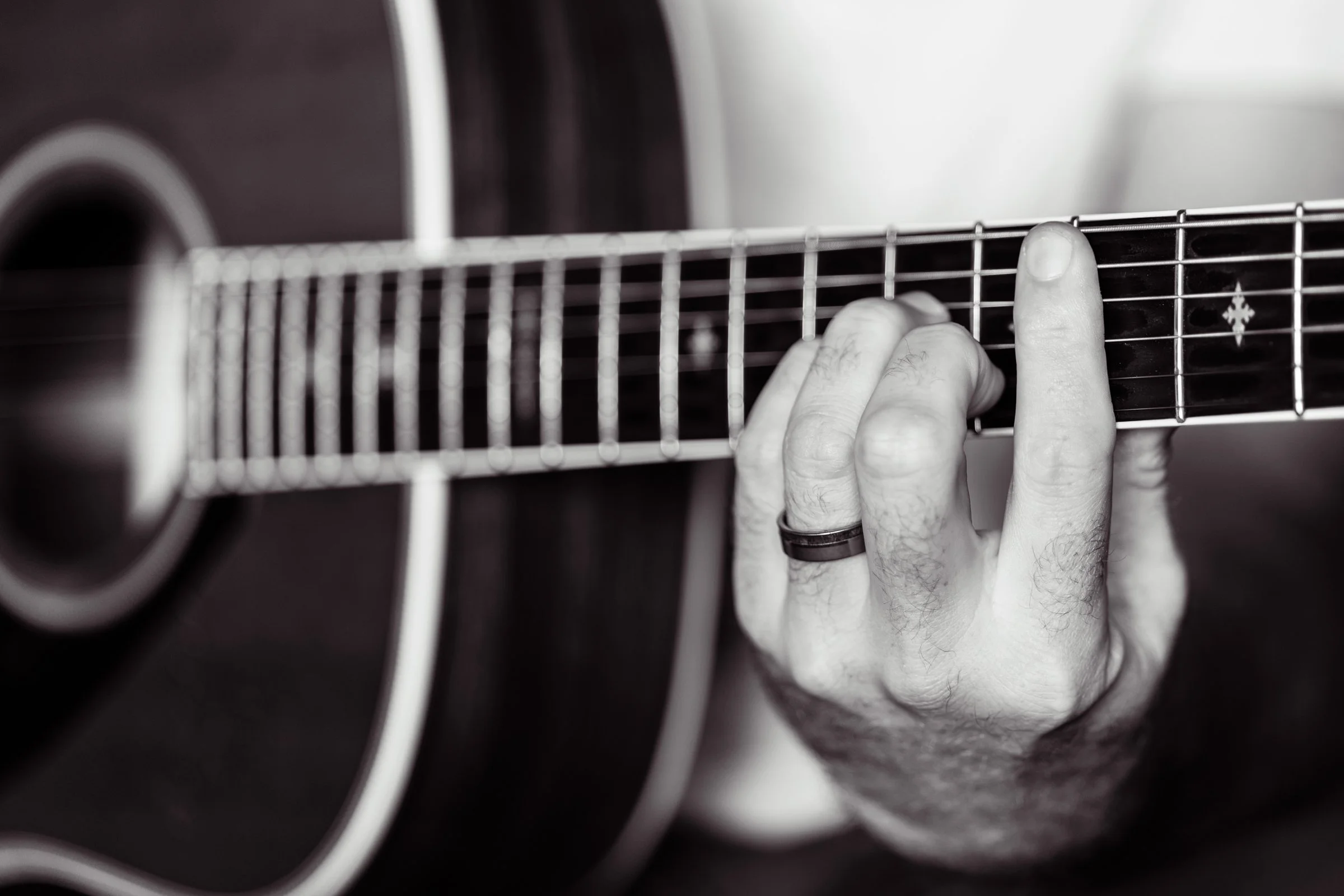 Close-up of a person’s hand playing an acoustic guitar, with fingers pressing on the guitar's fretboard.
