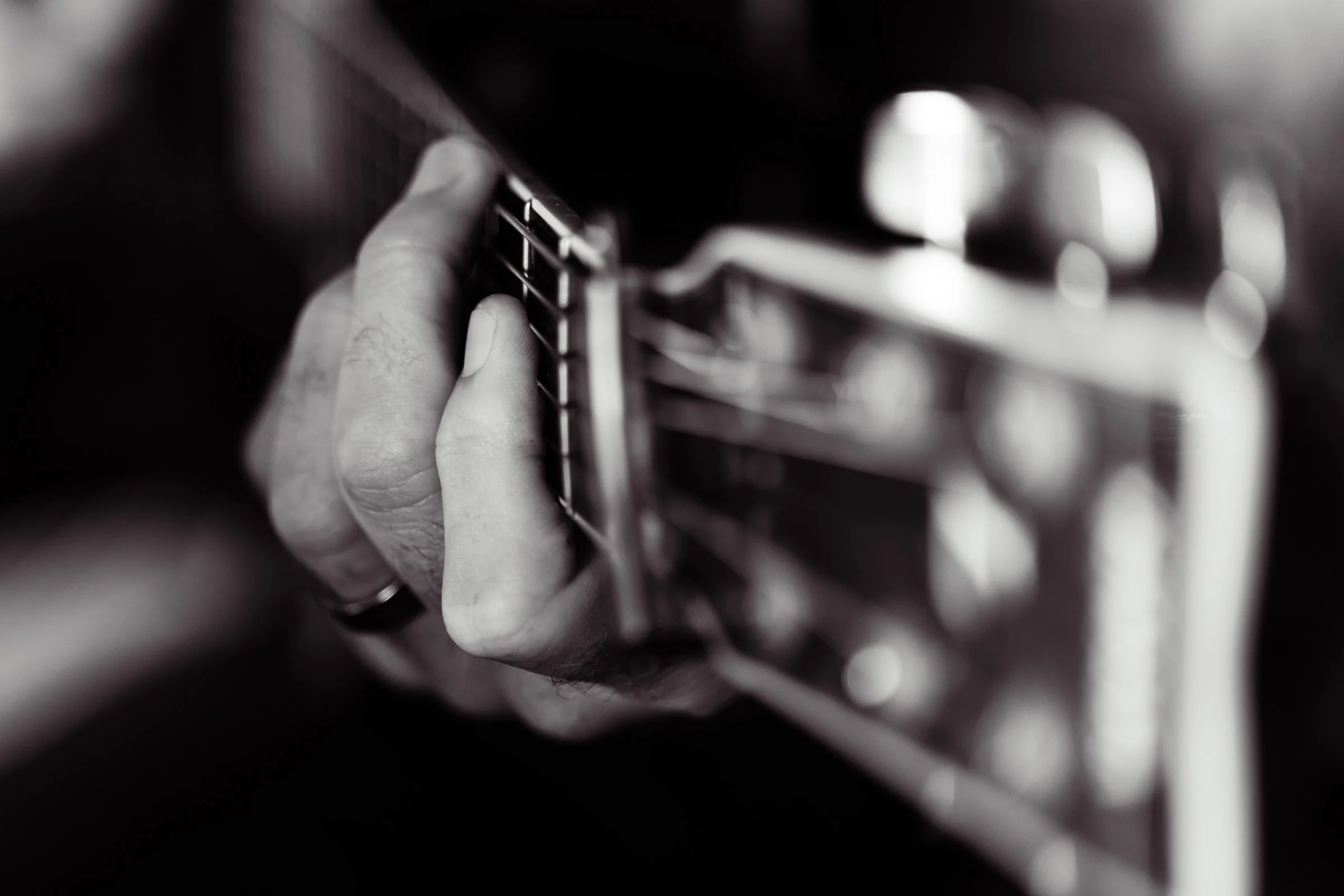 Close-up of a person’s hand playing a guitar, focusing on the fingers pressing the guitar strings.