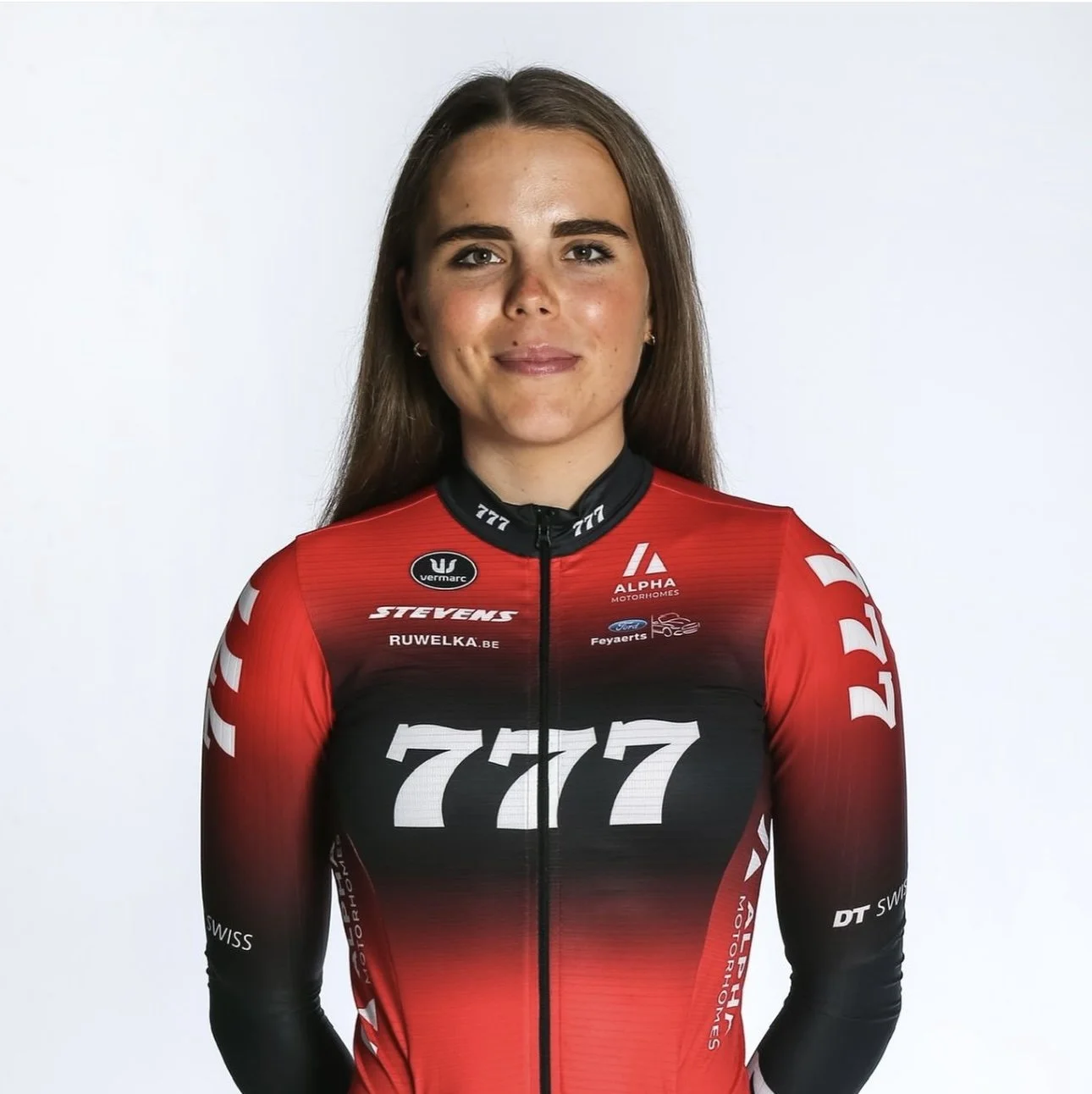 A woman in a red and black cycling jersey with the number 777, smiling slightly, standing against a plain white background.