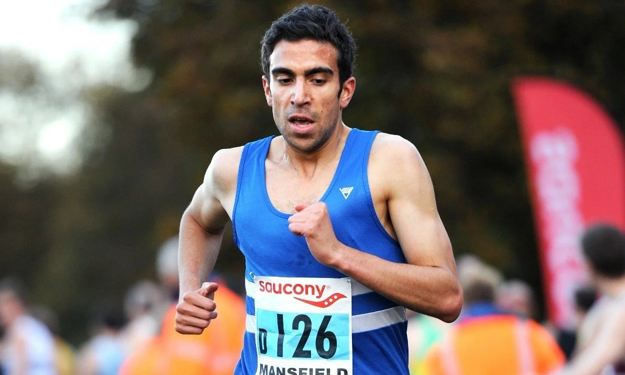 A male runner wearing a blue athletic tank top with a race bib number 126 running in a race event.