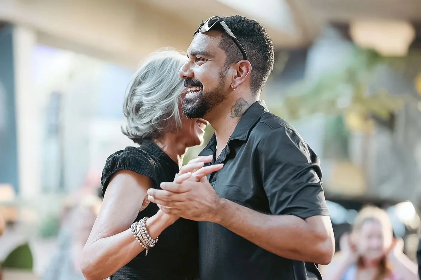 People dancing closely in pairs in a dance studio with brick walls and large windows.