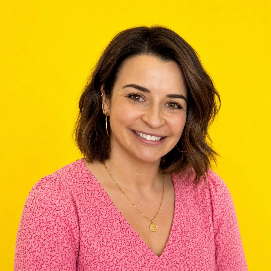 A woman with long black hair, wearing a checkered shirt, gold hoop earrings, and a gold necklace, smiling against a bright yellow background.