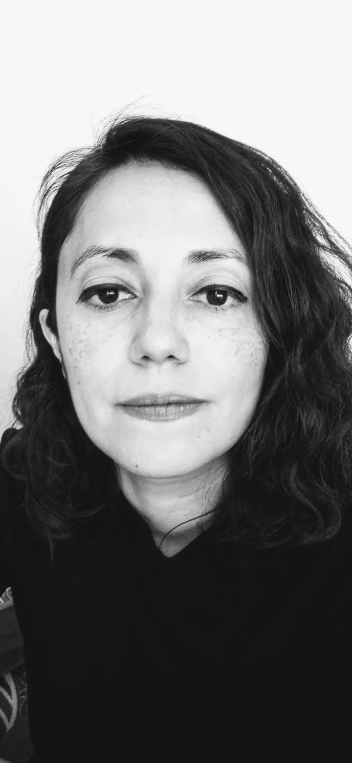 A black-and-white photo of a woman with wavy hair, looking directly at the camera with a slight smile.