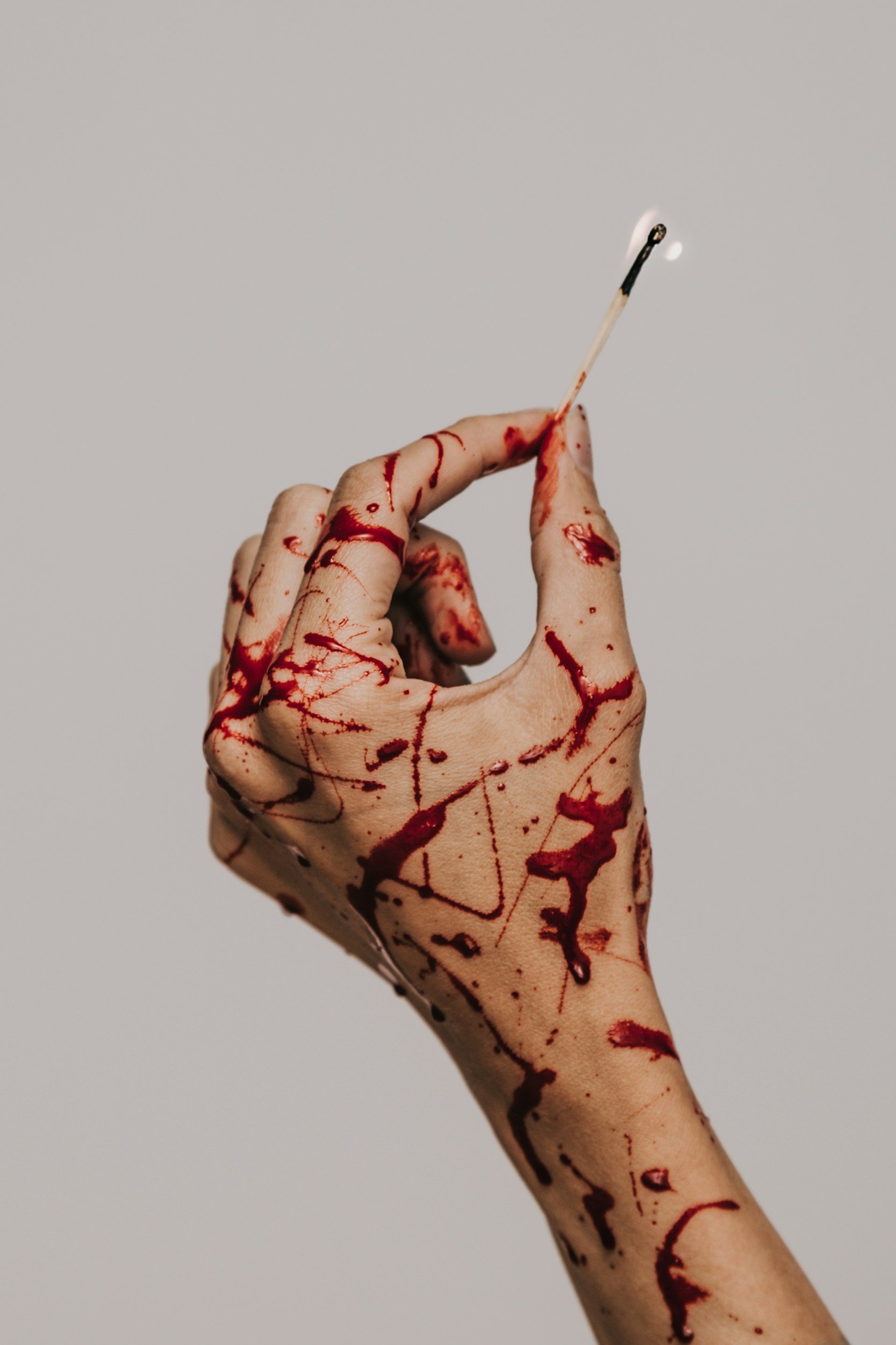 hand covered in blood holding a match