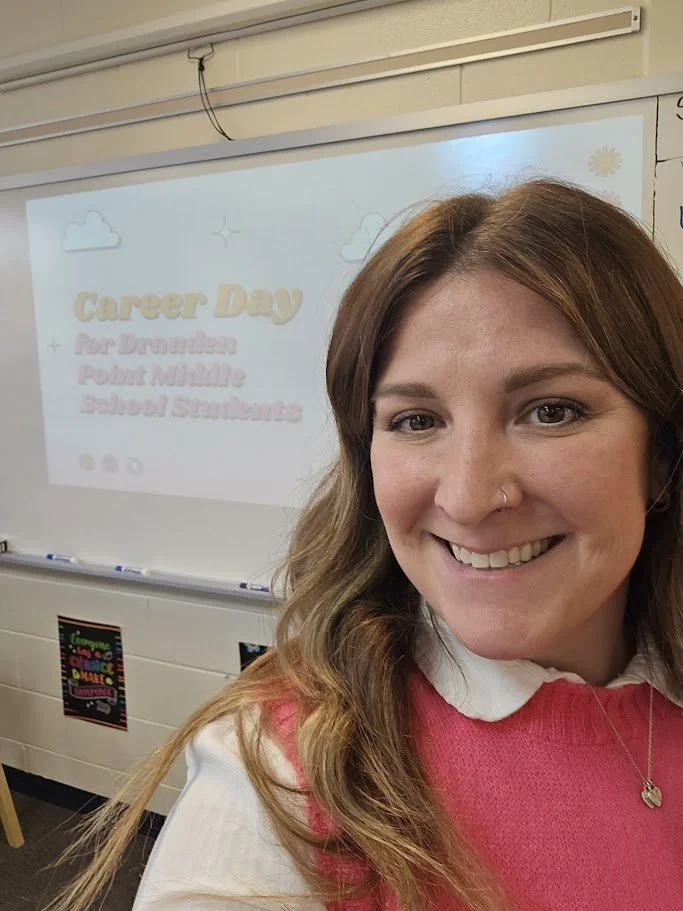 Alex smiling as she stands in front of a white board that is showing her presentation for Career Day.