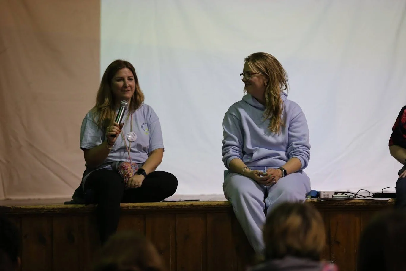 Alex and partner sitting on a stage in a relaxed state presenting at a school.