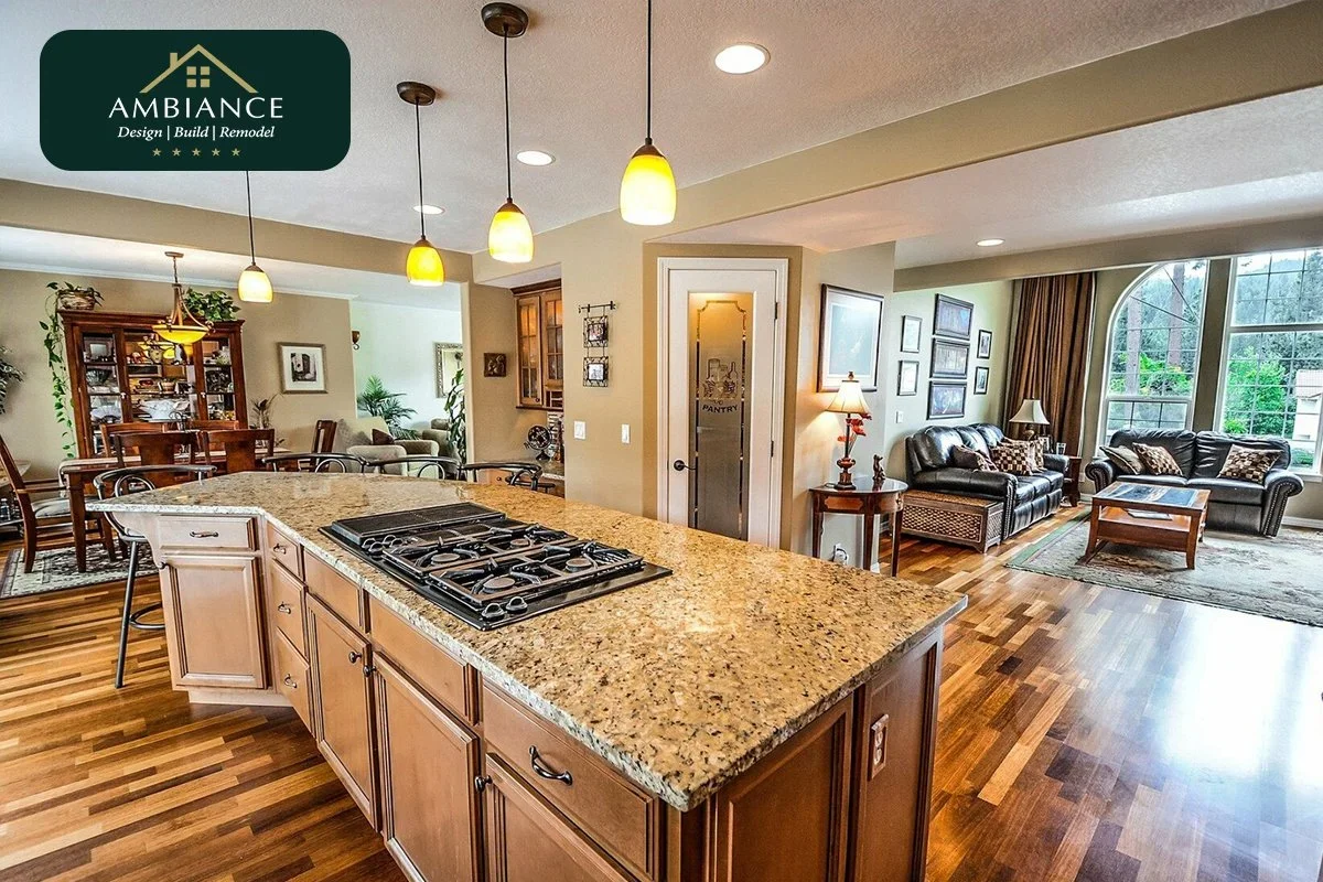 Open-concept living room and kitchen with granite countertop, hardwood floors, leather sofas, large arched window, and pendant lighting.