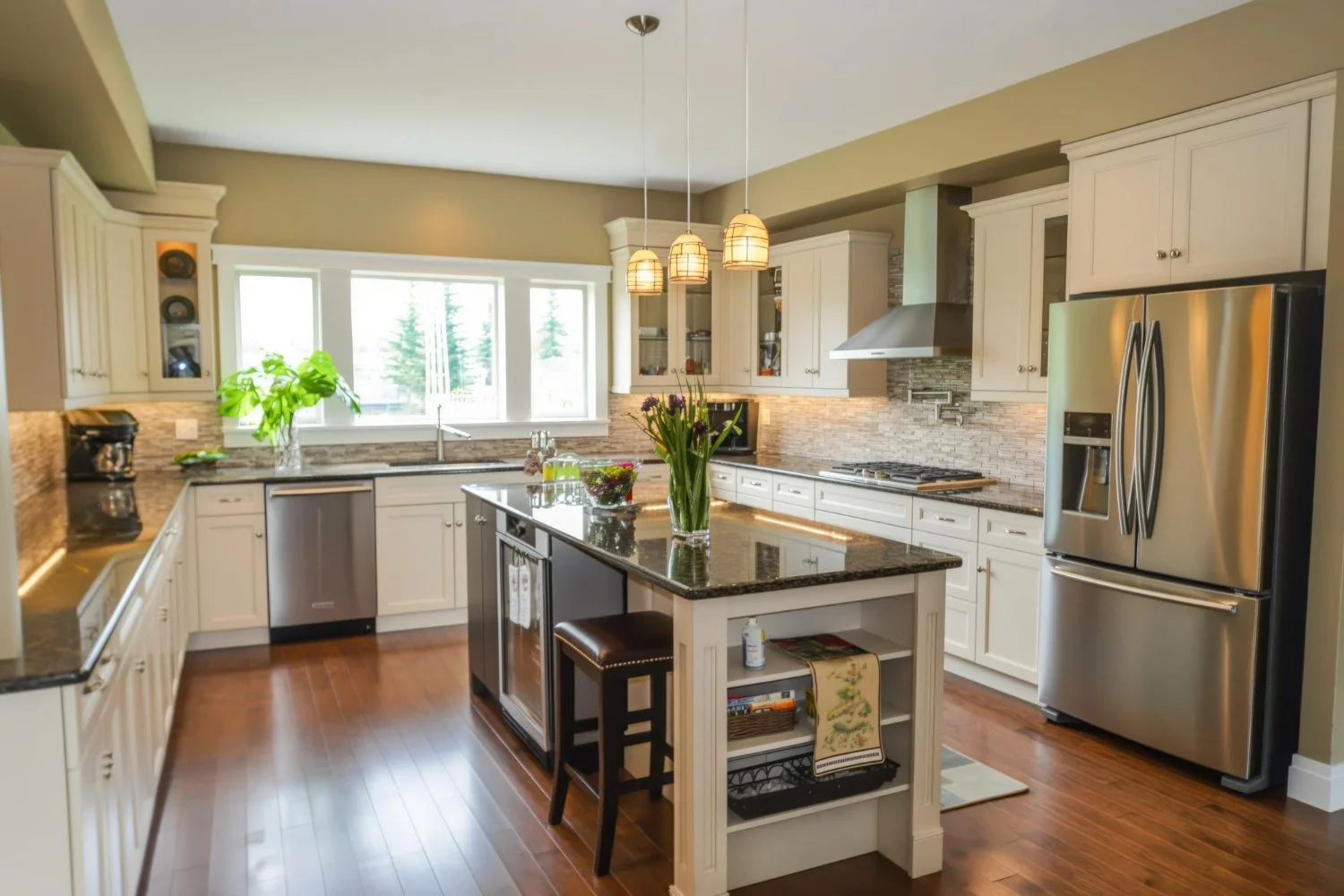 Modern kitchen with white cabinets, black granite island, stainless steel appliances, hardwood floors, and pendant lighting.