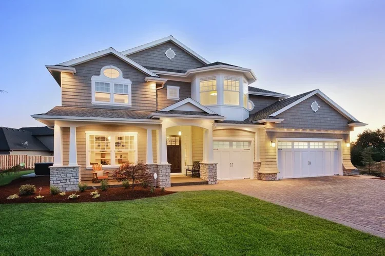 Exterior view of a large, two-story modern house with a well-maintained lawn, a walkway, and a stone porch at dusk.