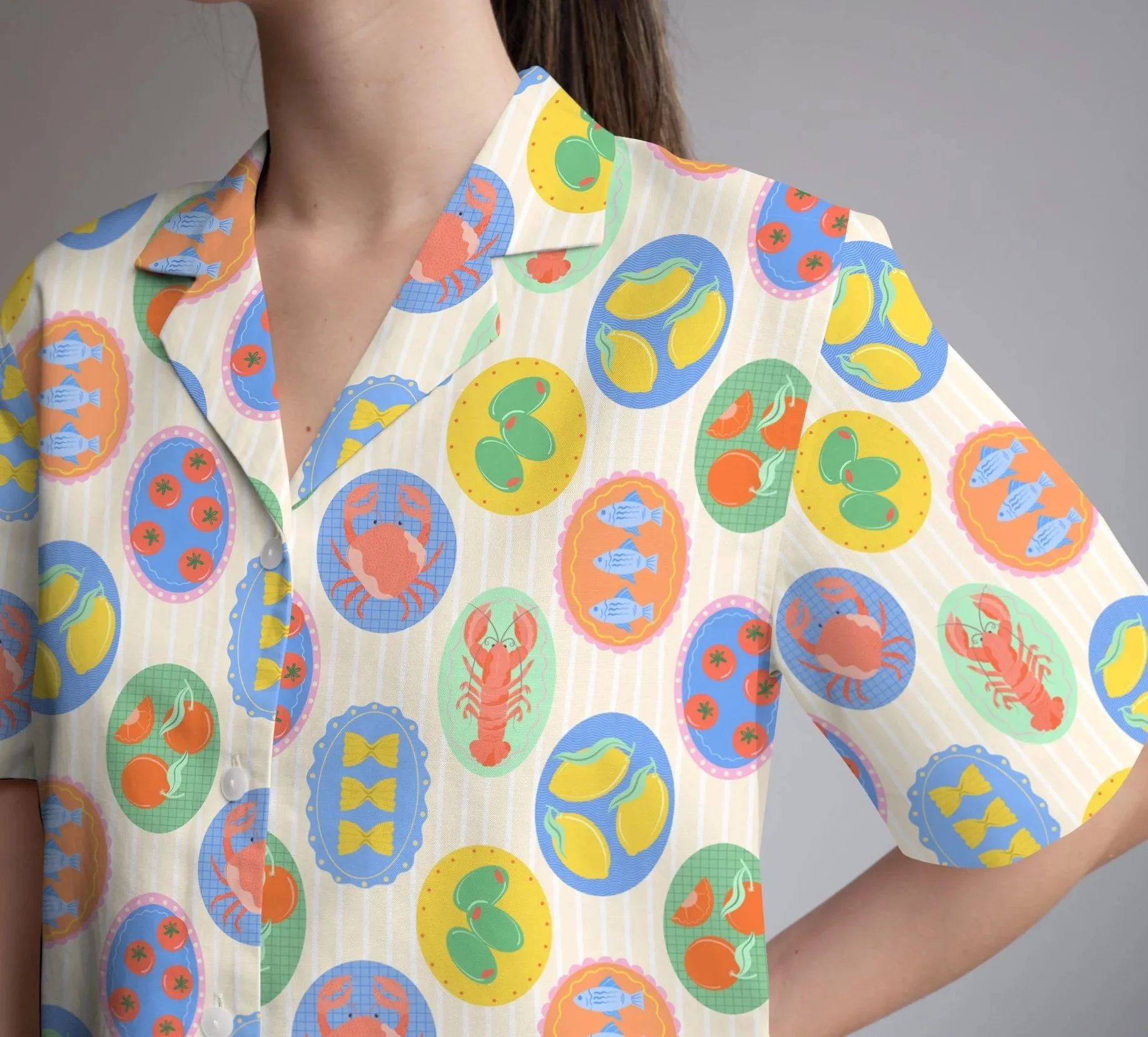 Person wearing a shirt with a colourful pattern of fruits and seafood, including lemons, tomatoes, and lobsters.