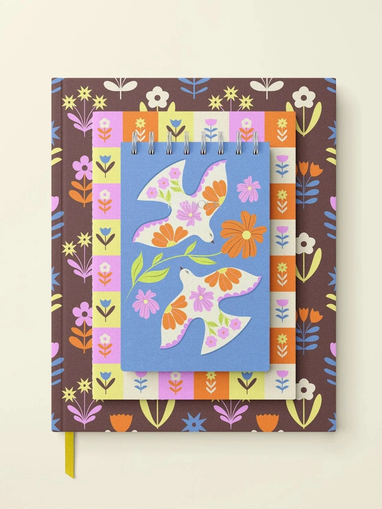 Colourful floral-themed notebook with a spiral-bound mini notebook on top, featuring two butterflies with flower patterns on their wings, set against a multiple-layered, patchwork background of floral prints.