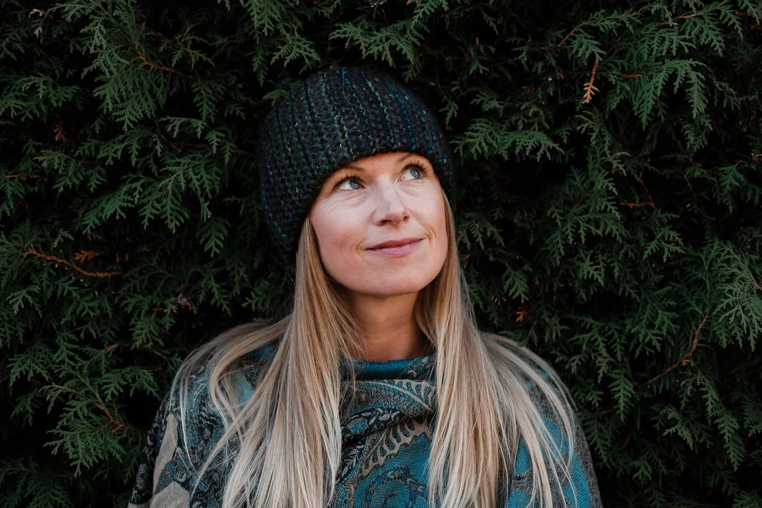 Portrait of photographer Sarah Bach in a green beanie against a background of dark green trees.