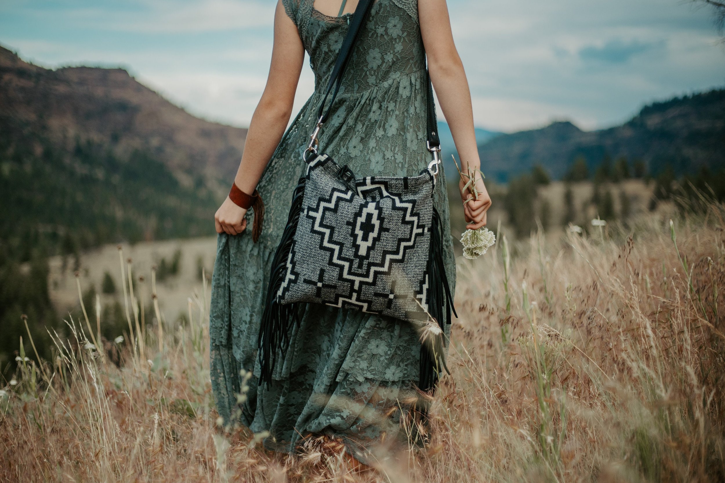 woman standing in a meadow with a native inspired purse in a black wool and black leather
