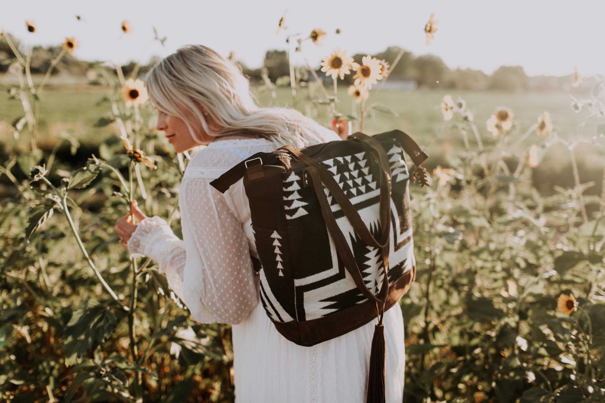 woman smelling flowers wearing a diaper bag backpack in geometric native wool