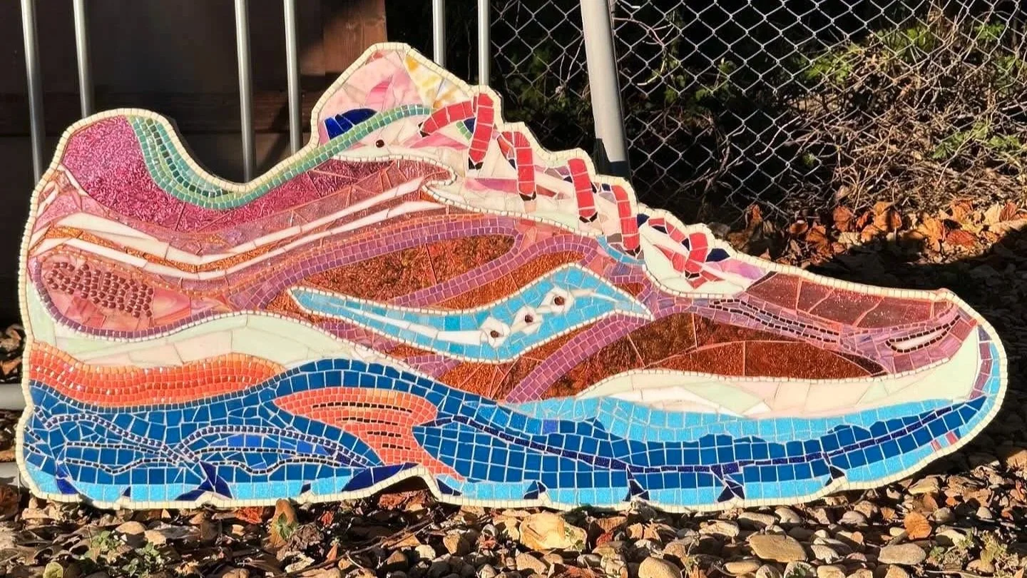 Colorful mosaic art piece of a Saucony sneaker, made with small tiles in pink, blue, brown, and white.