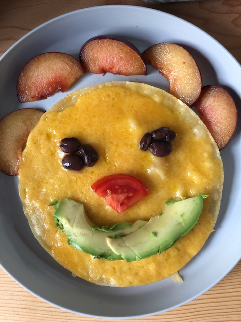Happy face tostada with cheese, beans, tomatoes, avocado, and fresh plums